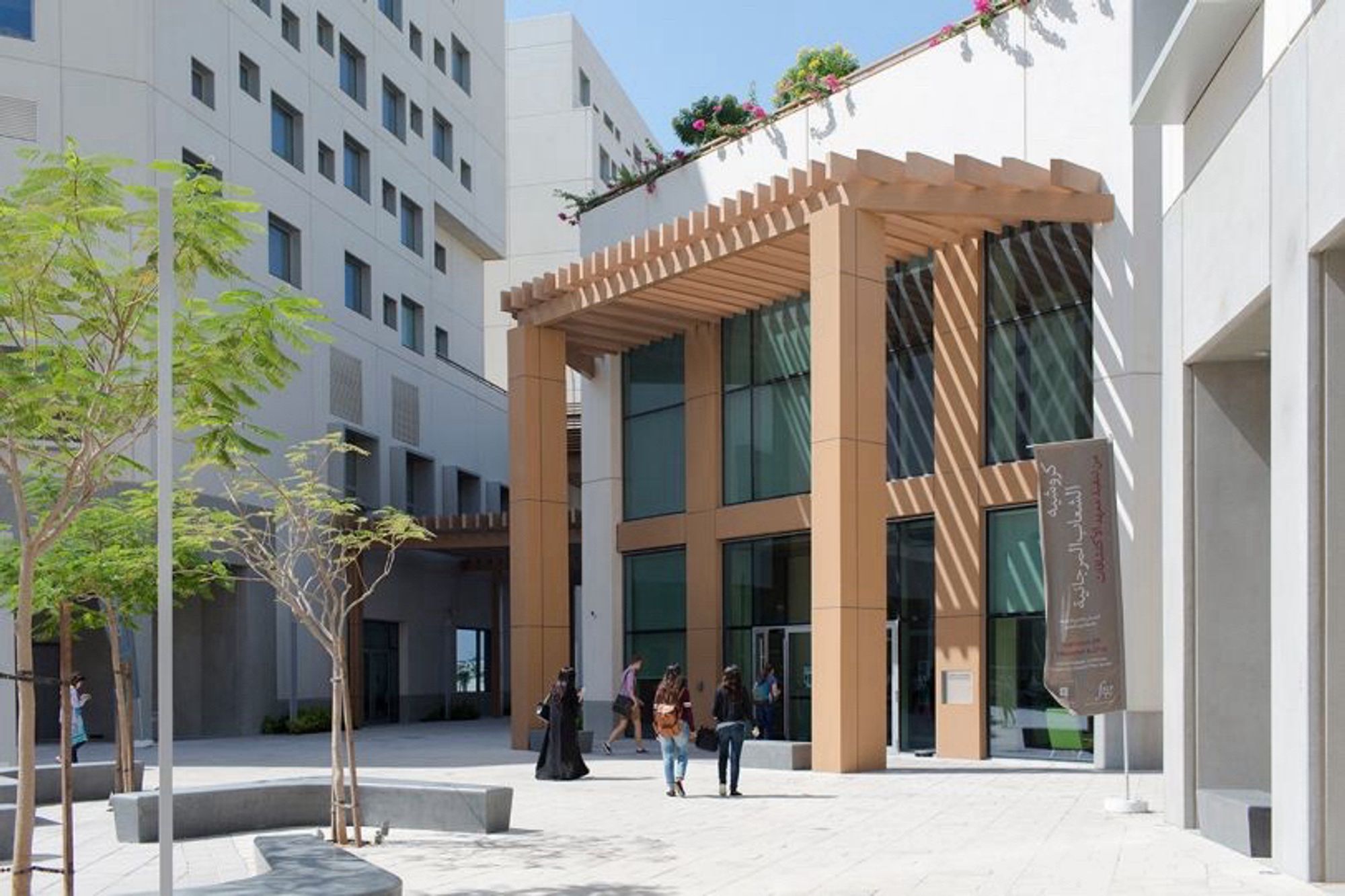 An image of an NYUAD campus building in a sunny courtyard where a few students and faculty are walking by.