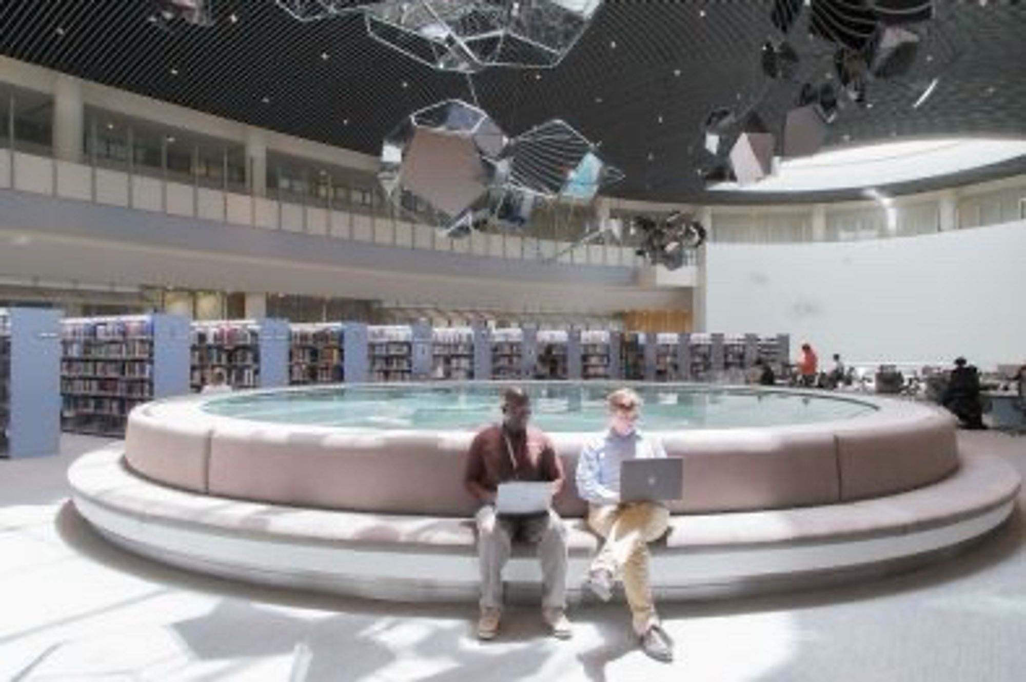 Two scholars write together on laptops, sitting side by side, in the NYUAD library.