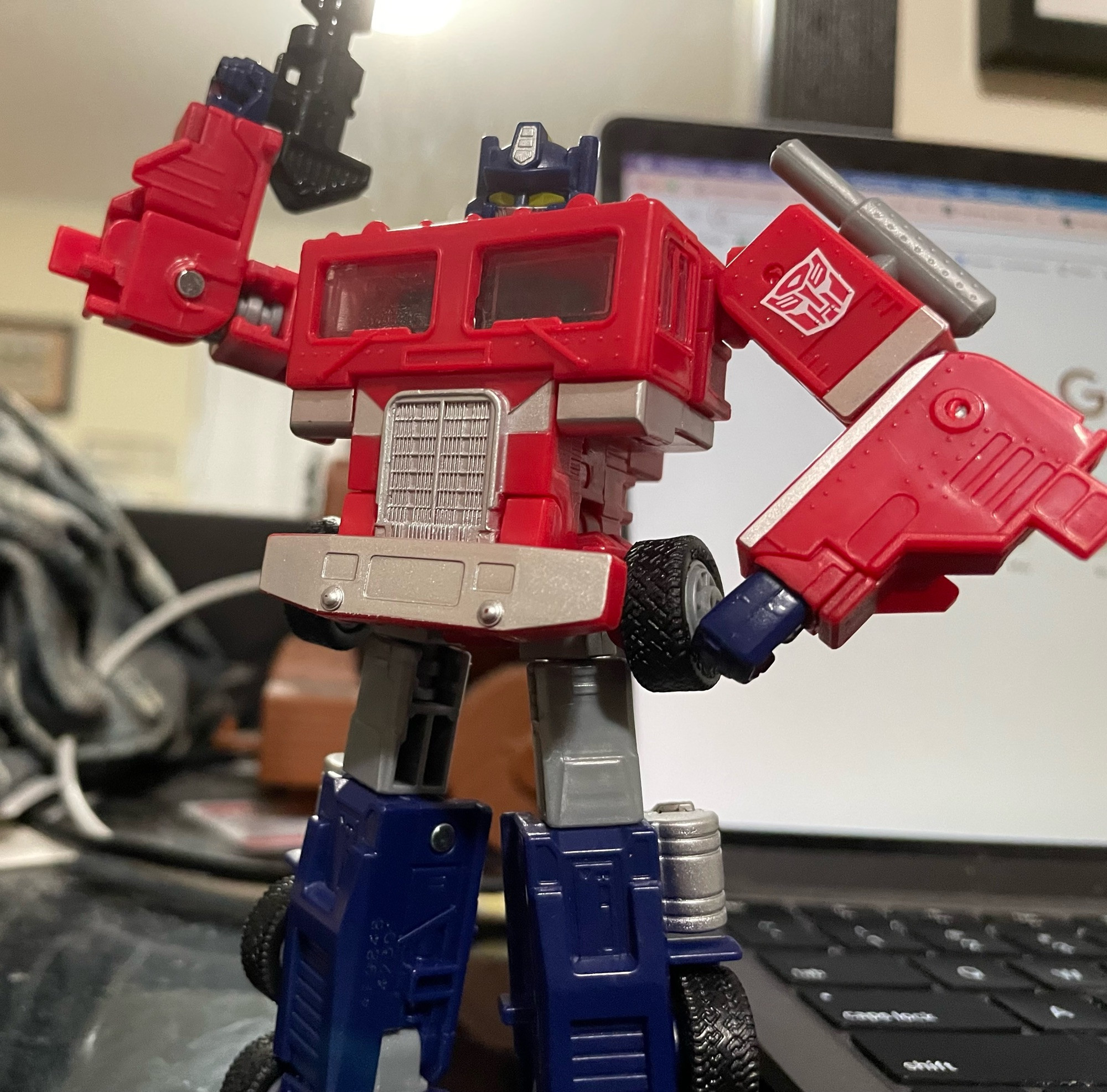 Optimus standing with his left arm akimbo and holding his blaster up with his right hand