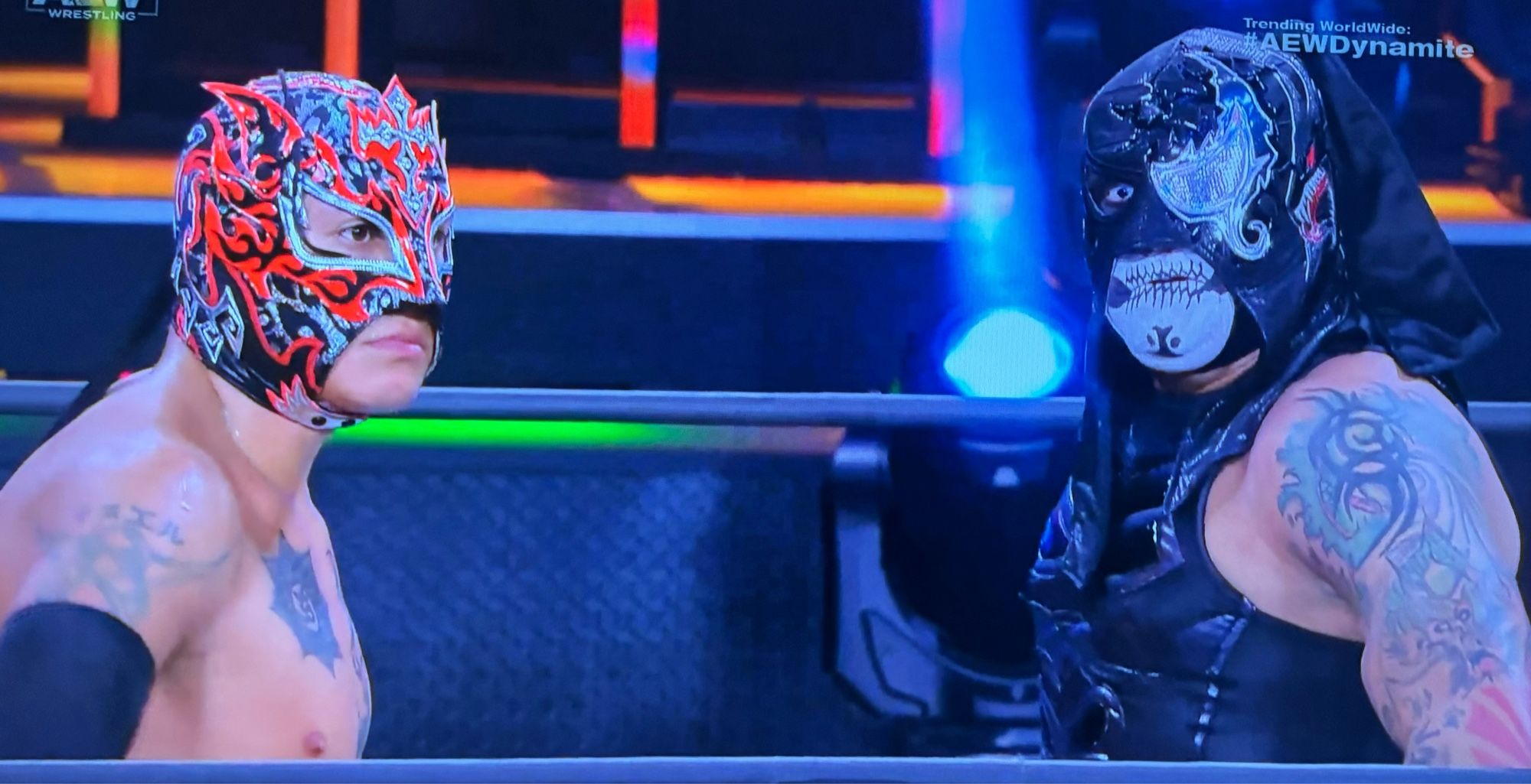 Rey Fenix (L) in a lovely red, silver and black mask and Penta (R) with a half-Venom mask, a Venom-like eyepatch over the left eye and the exposed right eye staring directly to camera