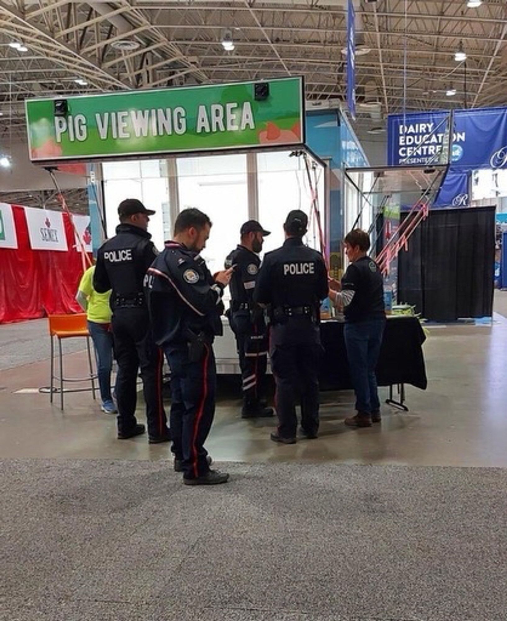 A group of uniformed police standing under a sign (at a fair) that reads "Pig Viewing Area"