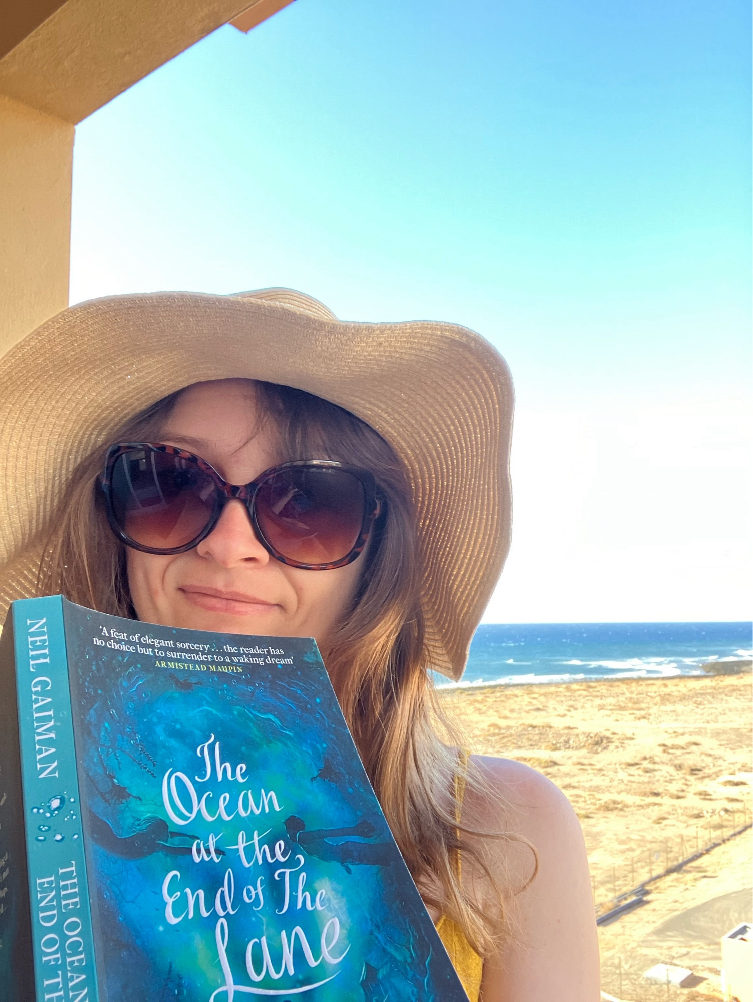 Me holding a book ‘ocean at the end of the lane’ on the balcony with the ocean behind me.