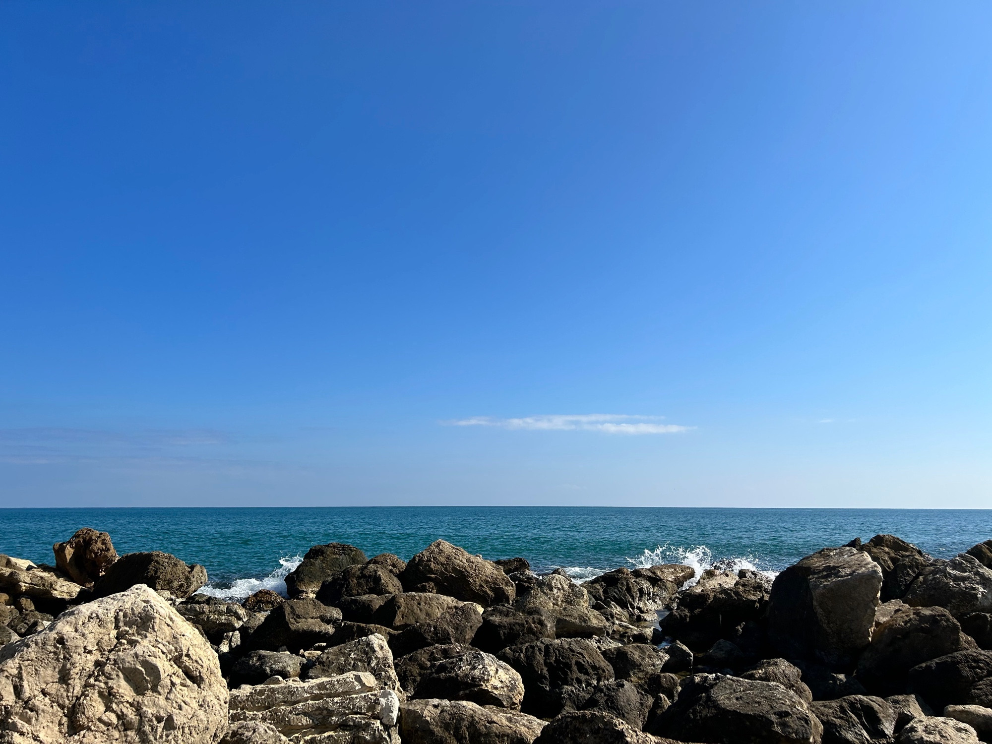 Espigon al que le da una ola de frente, puede verse el mar y el cielo de fondo