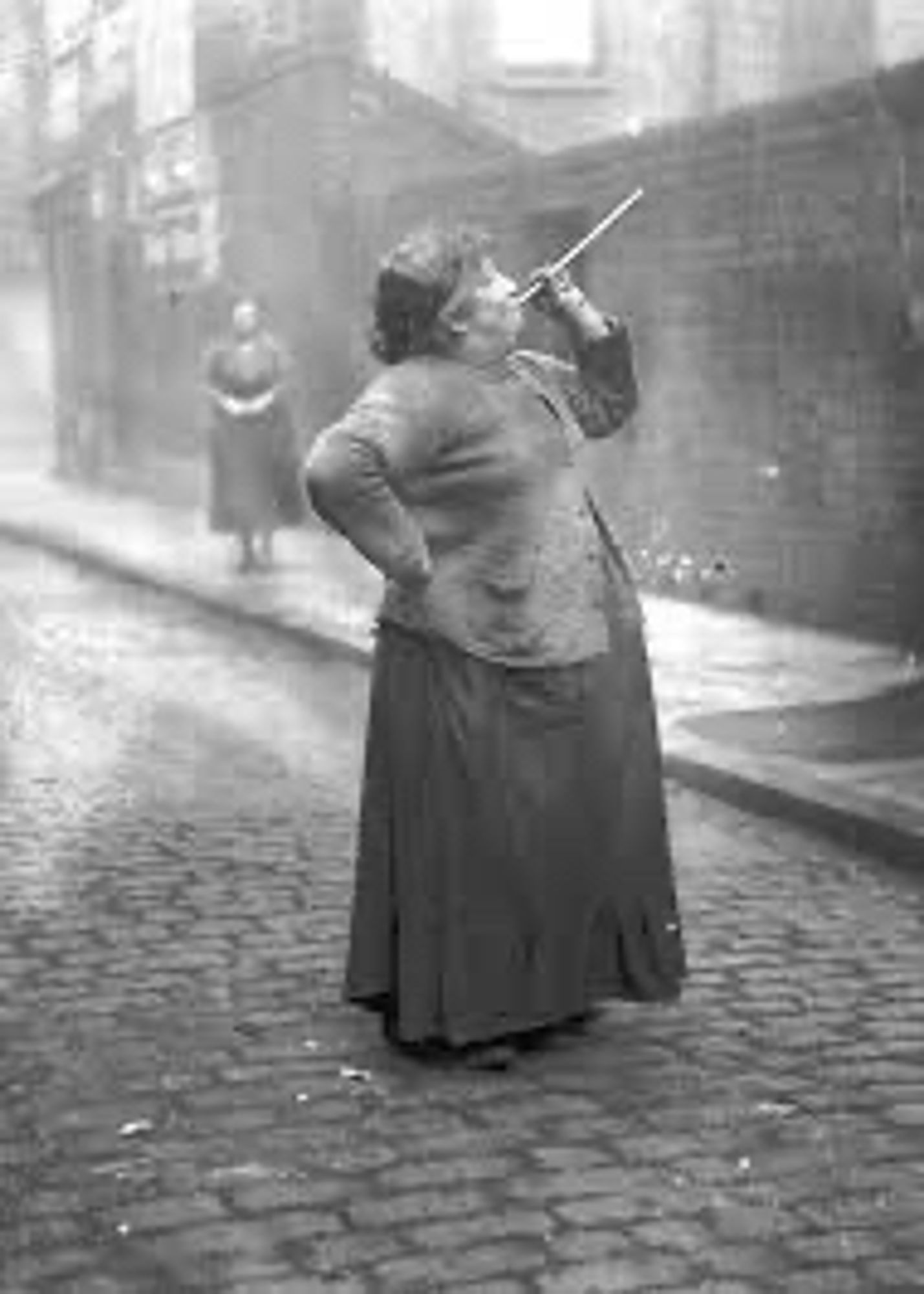 Mary Smith auf einer Straße. Rechte Hand in die Hüfte gestützt, in der linken Hand ein Pusterohr