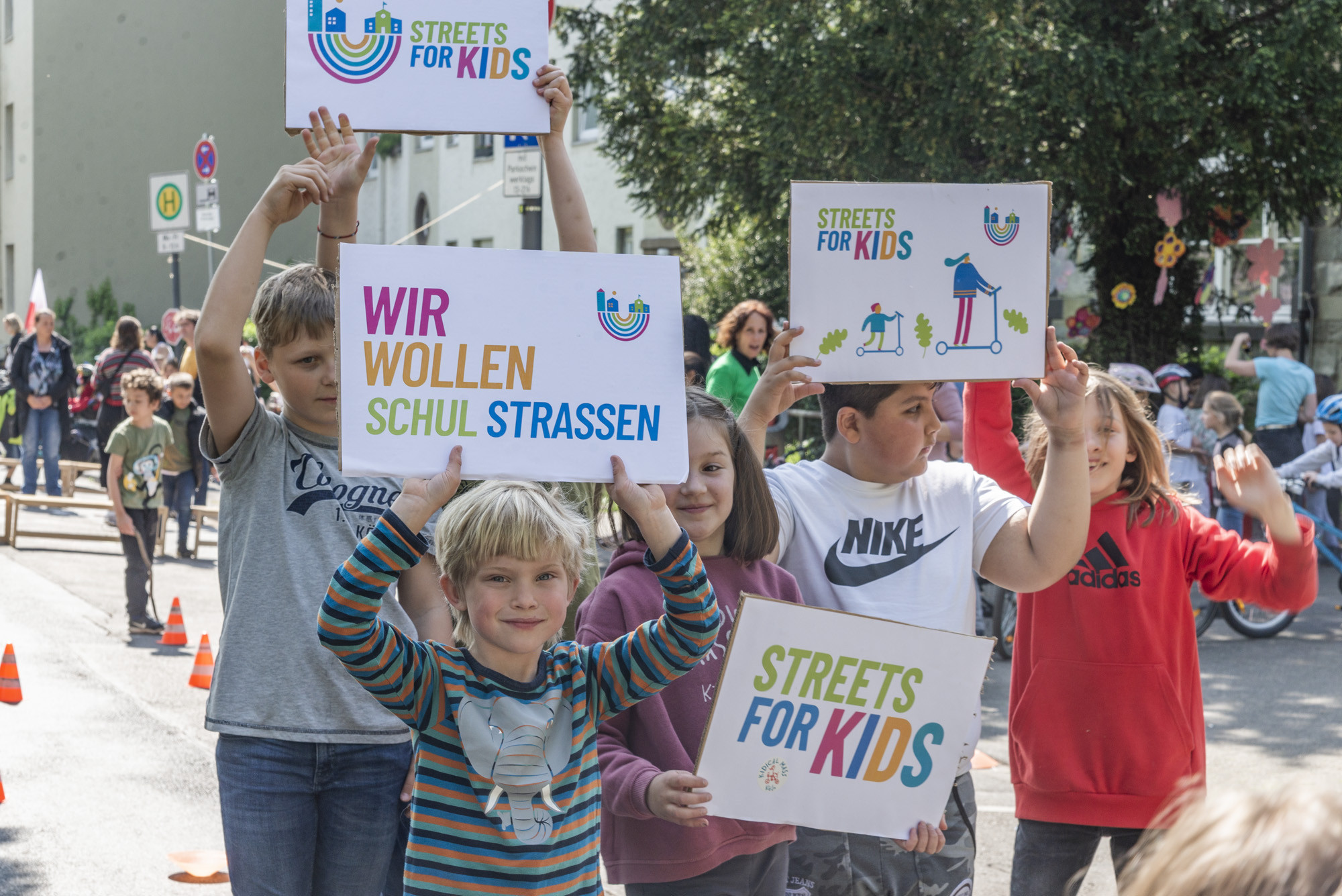 Bild mit Kindern auf einer Schulstraße mit Pappschildern in der Hand. Auf einem steht Wir wollen Schulstrassen.