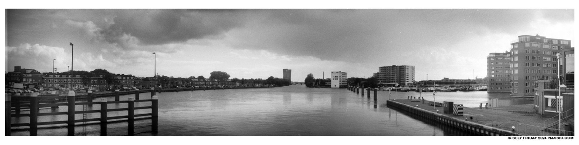 Black and white panorama of an expanse of water surrounded by buildings and docks.