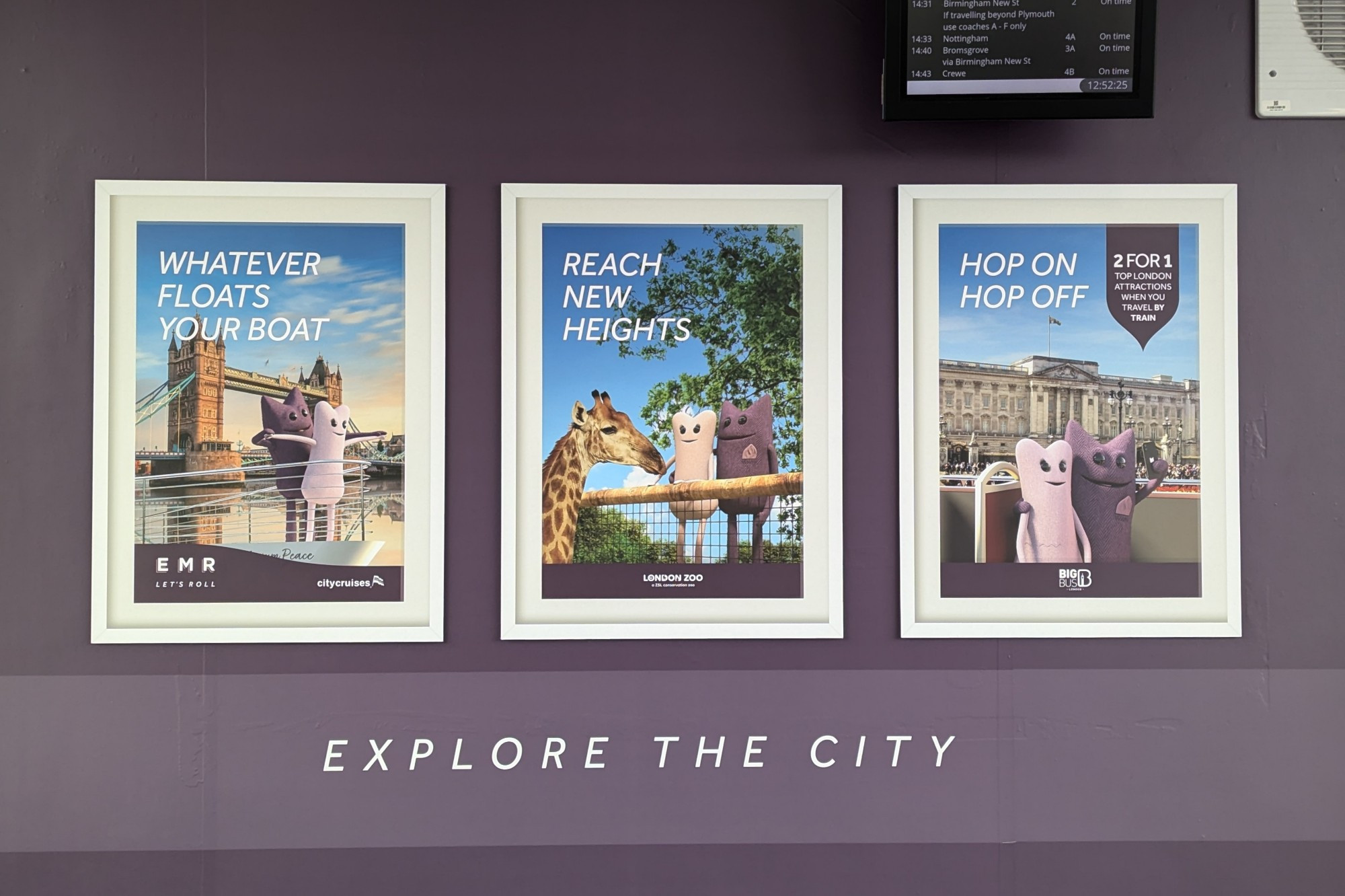 Three framed ads by East Midlands Railway featuring their mascot (a purple anthropomorphic creature) visiting various London landmarks with another pink anthropomorphic creature. The pink creature is smaller, rounder and has got eyelashes.