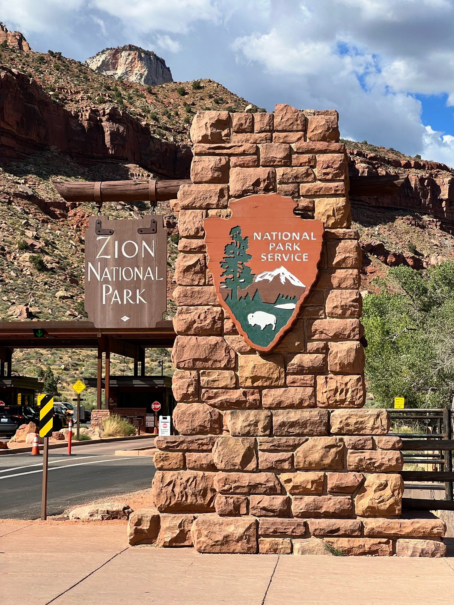 The Zion National park sign in Utah is like a little inverted spade ♠️ on red brick 🧱 facade that makes part of the controlled entrance. It’s so beautiful. There’s a little hill right behind it. I went in the summer, so it was hot and sunny 🌞. 