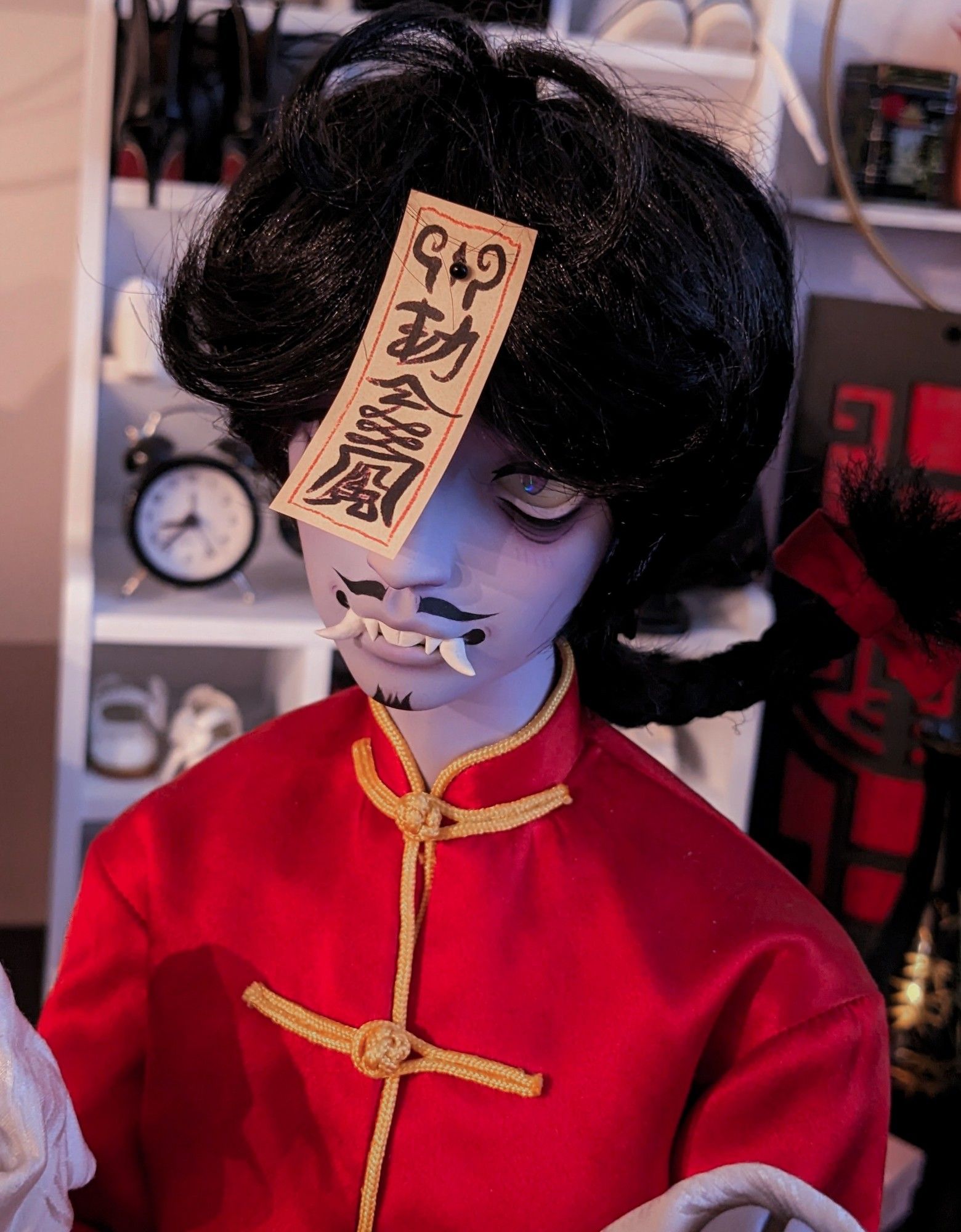 a close up of Yun's face.

He is a Chinese hopping vampire, or 僵尸. His skin color is a ghostly  purple hue. He is wearing a red tang suit with gold duck buttons and trim. His hair is black and messy looking with a braid at the back. His eyes are sunken and deathly, his exposed teeth have sharp protruding fangs, and a mustache and small beard adorn his face. He has a magical talisman attached to his forehead to keep him docile.