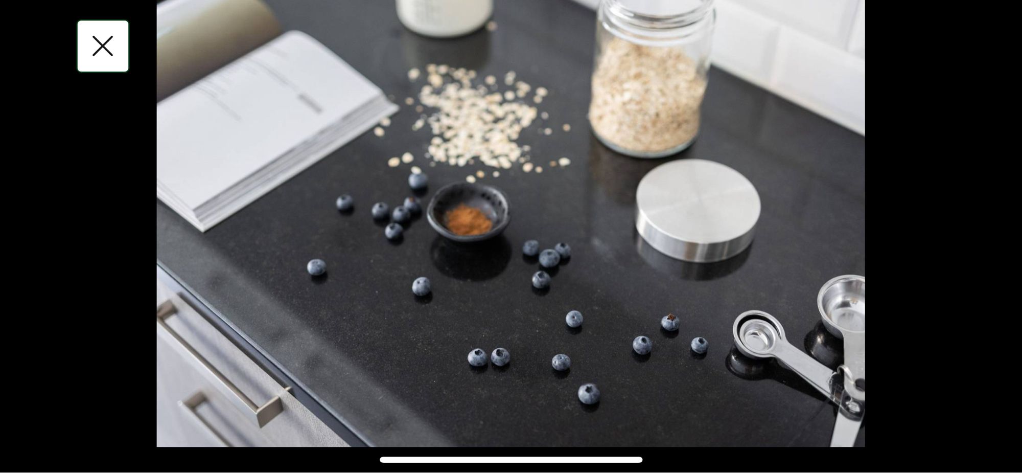 Blueberries and out of focus oats(??) spilled on a dark kitchen counter. Clean measuring spoons and a small dish of powder that looks like cinnamon. Also out of focus. So dumb.