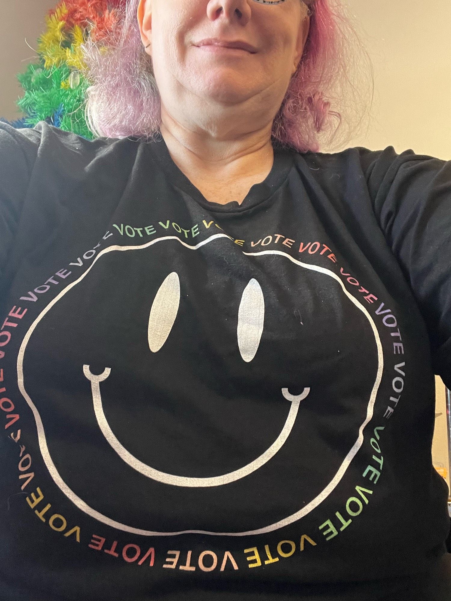 Black t shirt with a white happy face surrounded by repeated instances of the word VOTE in rainbow colors.