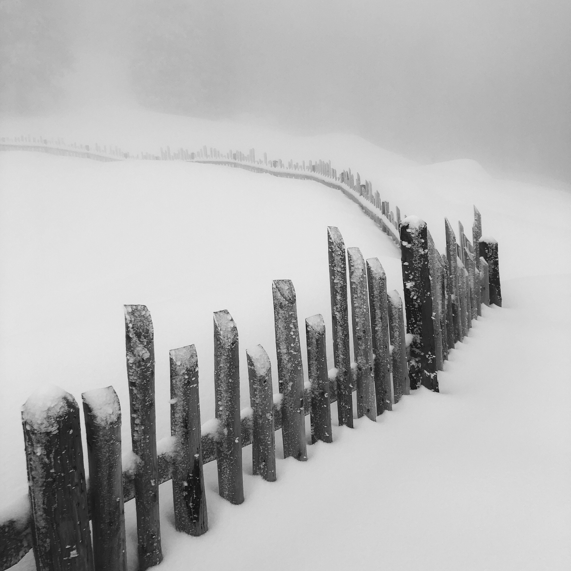 Un lungo steccato in montagna con nebbia e tanta neve