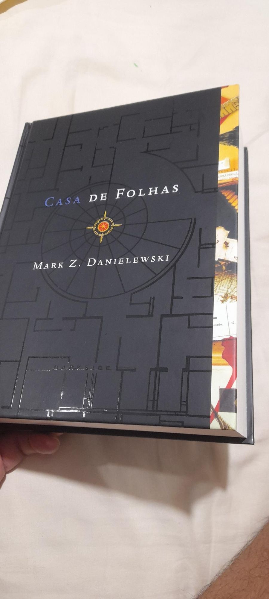 Livro de capa dura predominantemente preto com detalhes geométricos diversos cujo título é "Casa de Folhas" do autor "Mark Z. Danielewski"