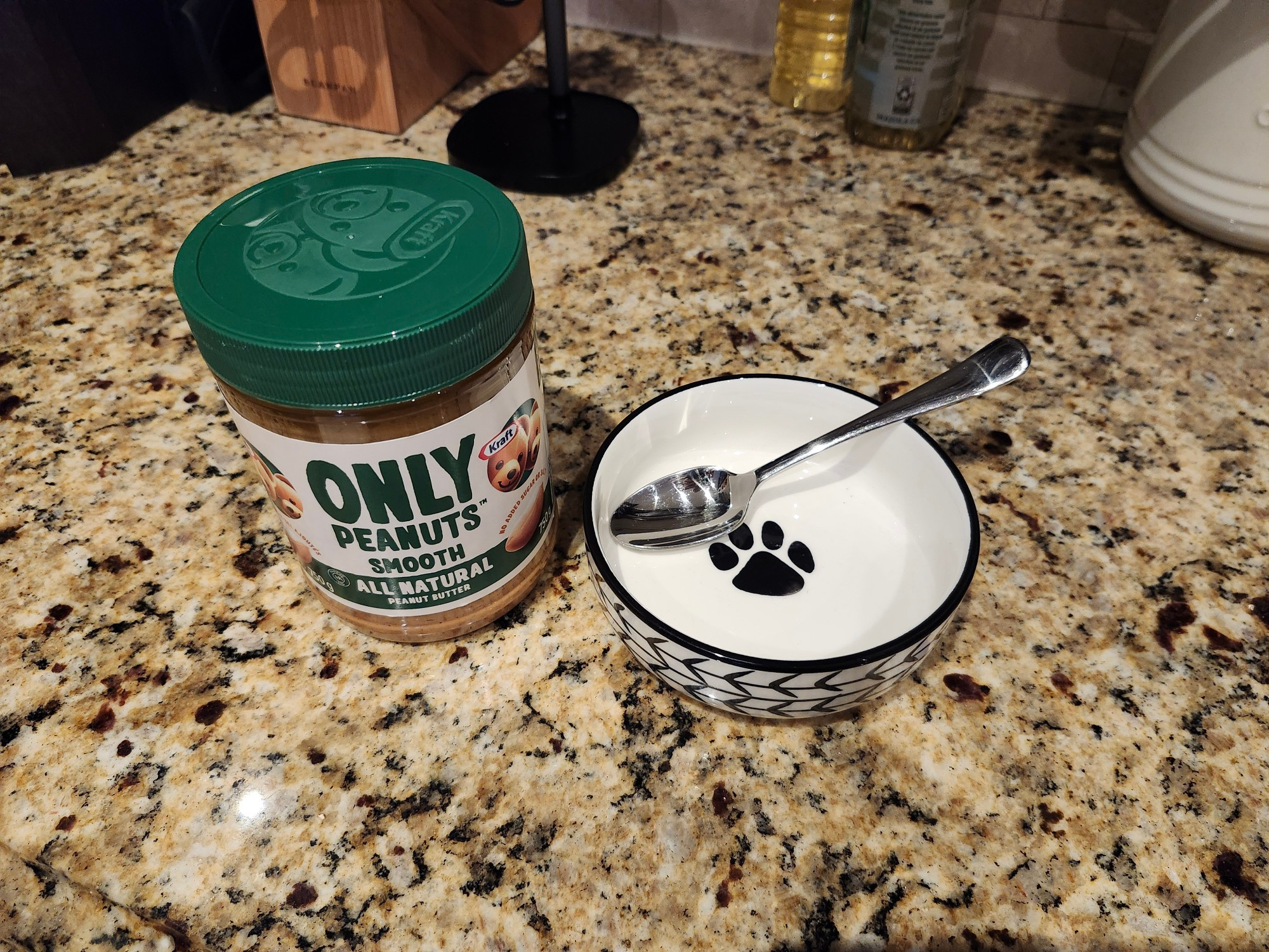 A jar of peanut butter next to a dog bowl with a spoon in it