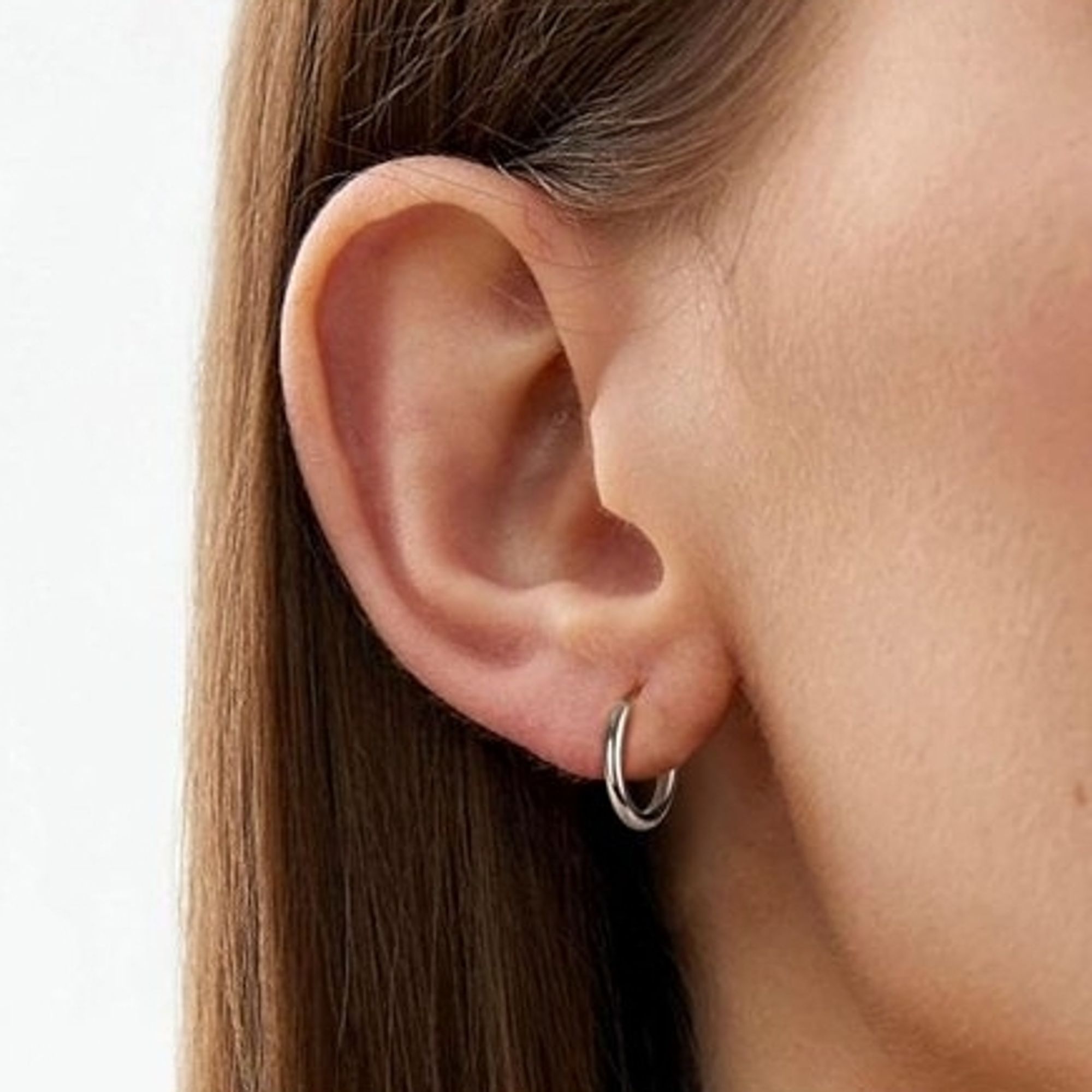 A woman's right ear with a small silver hoop earring on their earlobe