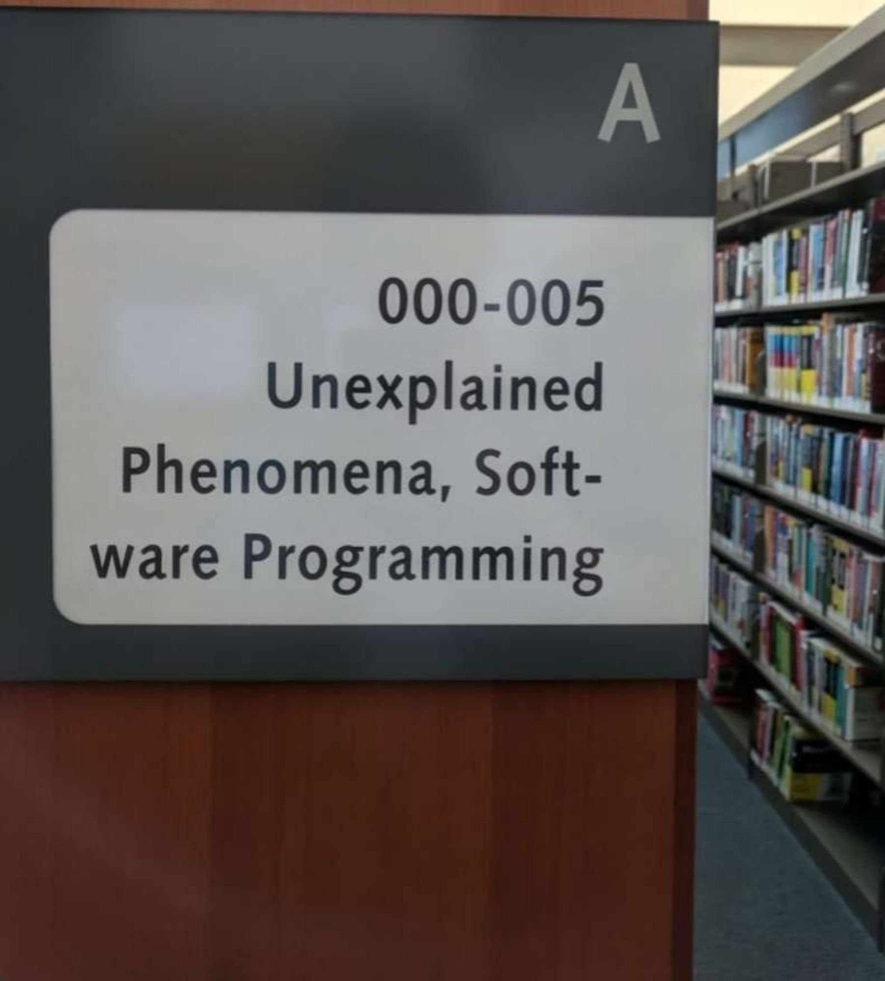 Library sign saying that the shelf contains books on unexplained phenomena, software programming