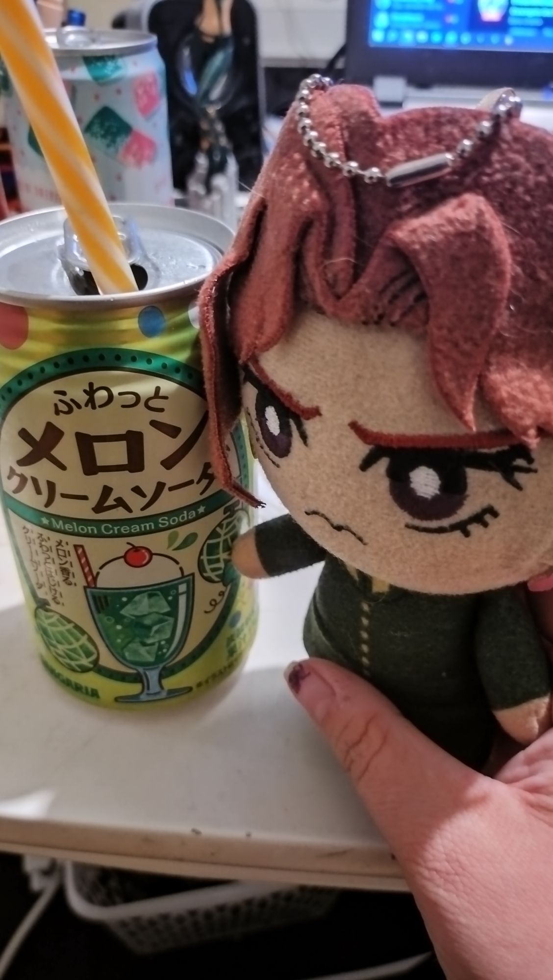 A plush of Noriaki Kakyoin next to a can of a melon cream soda with a straw sticking out of it.