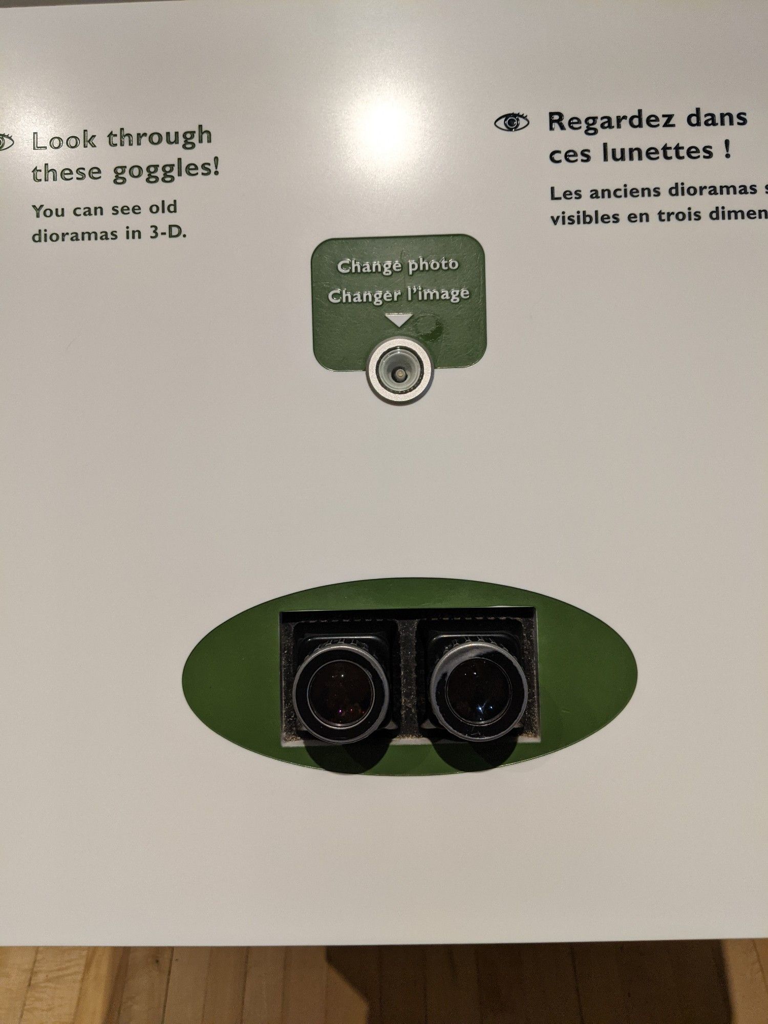 A museum exhibit with a stereo viewer and a button to change the slide. A sign says to look through the goggles to see old dioramas in 3-D