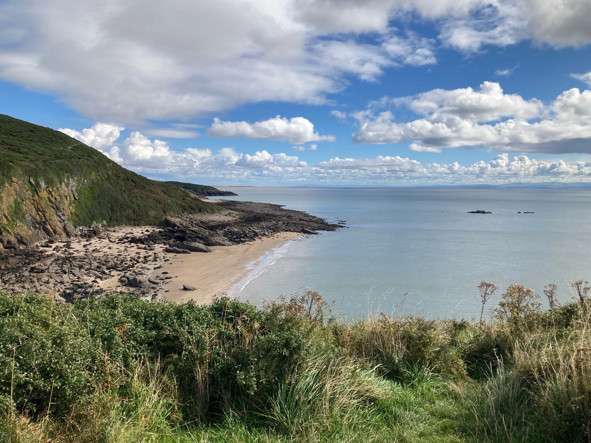 View of a beach and rocks from a cliff top view. Sunny sky with light clouds.