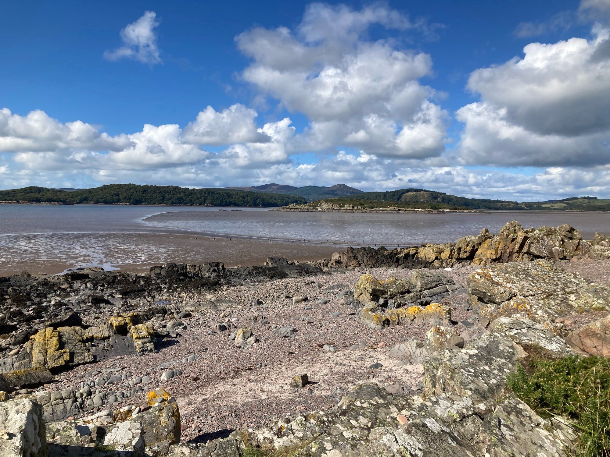 Rocky shore at low tide. Hills on the far side of the bay.