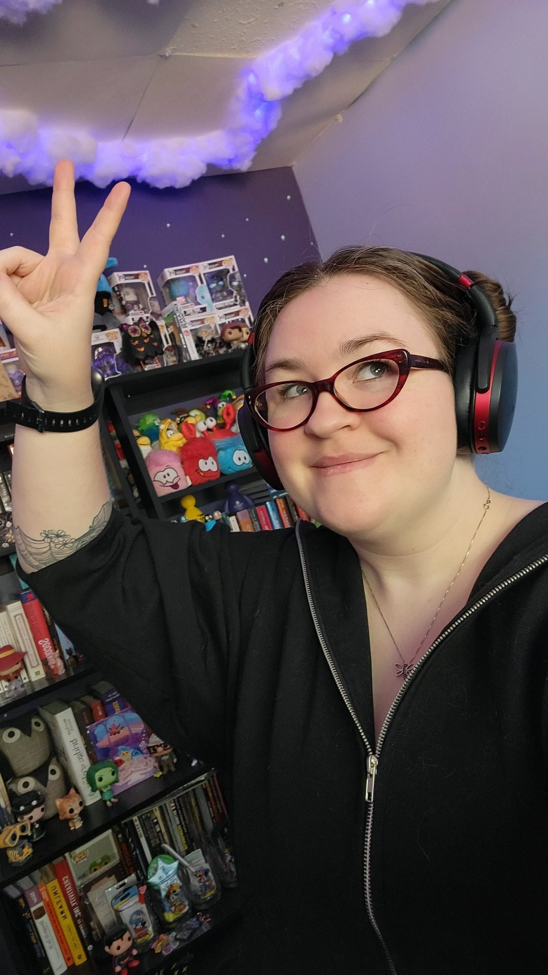 Amy throwing up a peace sign while looking off camera. She's in her office with full bookshelves behind her and glowing clouds on the ceiling.