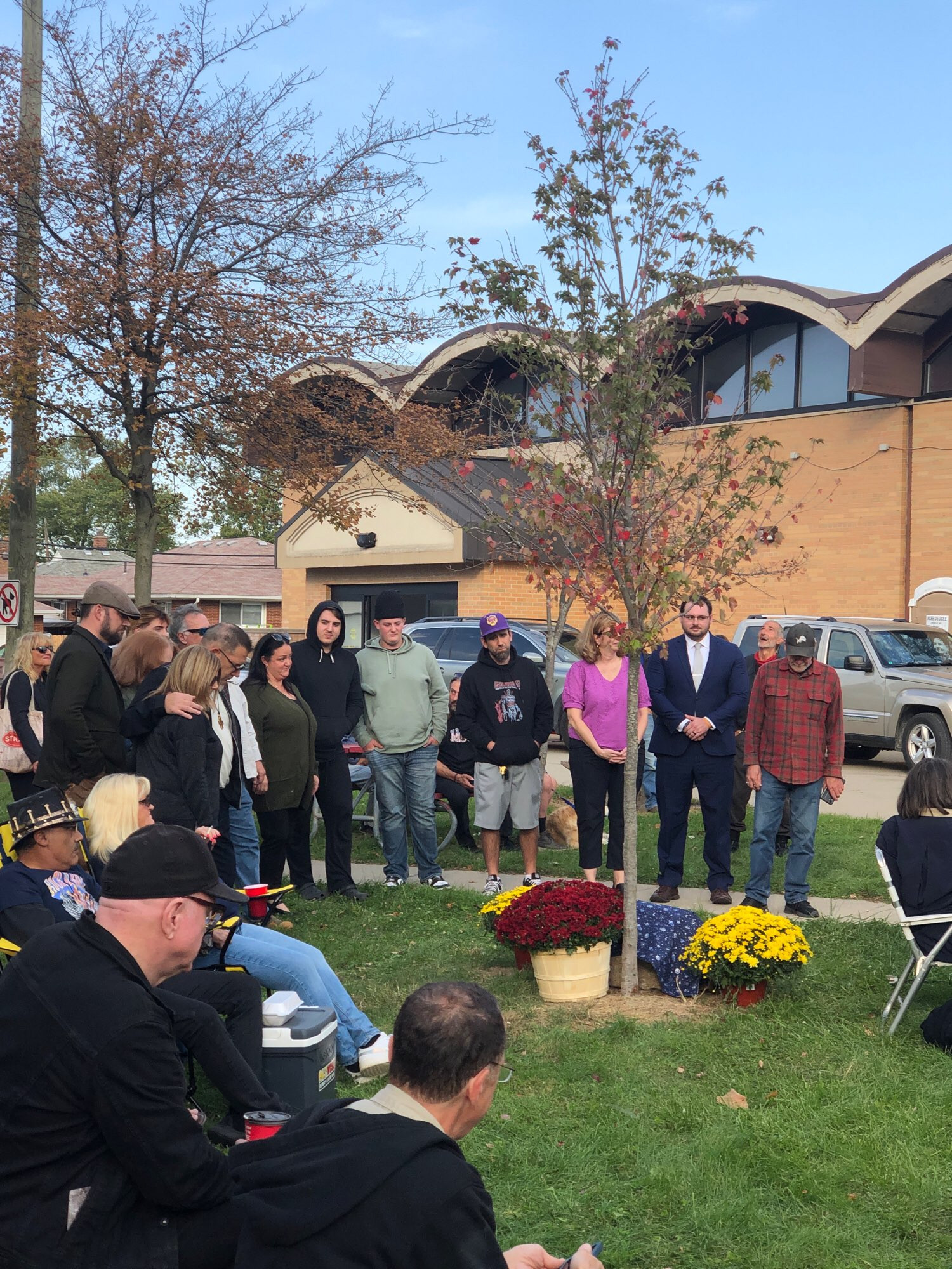 A crowd of people standing around a maple sapling