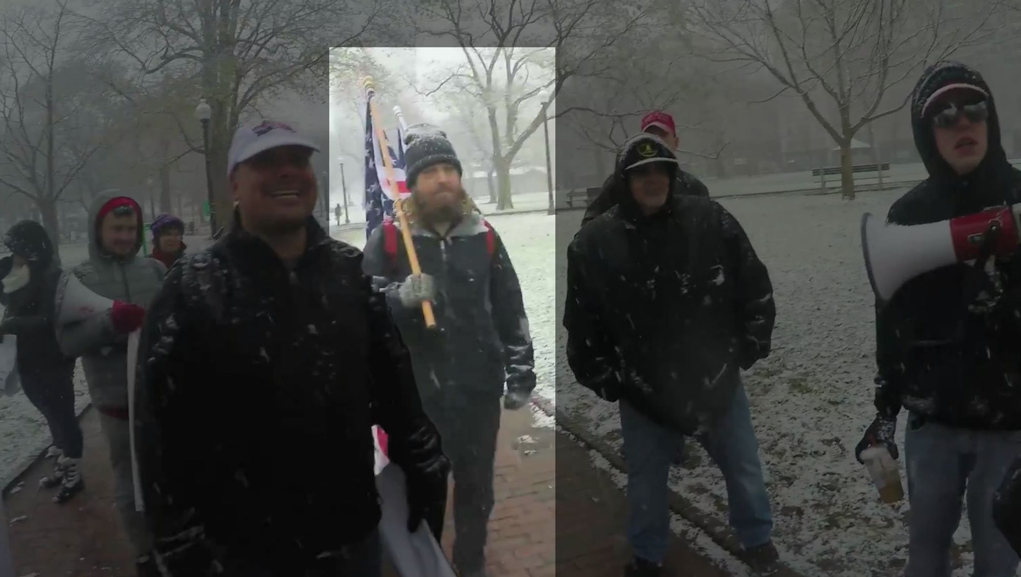 A still of video. It depicts several members of Resist Marxism in Boston Common, making their way from the State House to the Parkman Bandstand. Reihner, highlighted graphically, is among them. He wears the same clothes as the previous image, with a pair of black pants. With him, not highlighted, are Chris Bartley, Mark Sahady, Dan Gilby, and Mike Moura, as well as a smattering of other unidentified members. They've been stopped by member Garrett Kirkland, off camera. The brick walkway of the Common is visibly damp with melted snow. The surrounding grass is dusted with fresh snow.