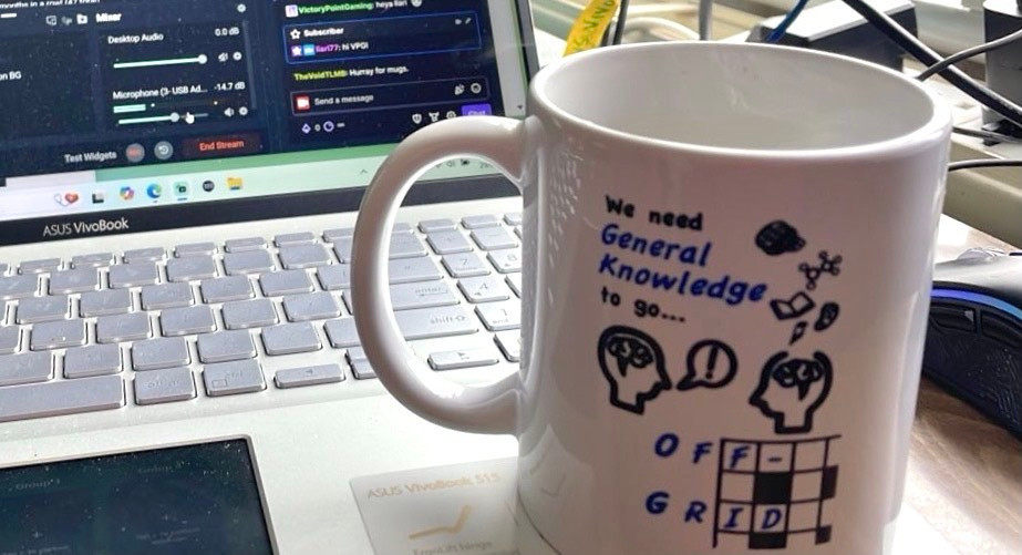 An Off-Grid logo on a white mug, resting on a table in front of a laptop.