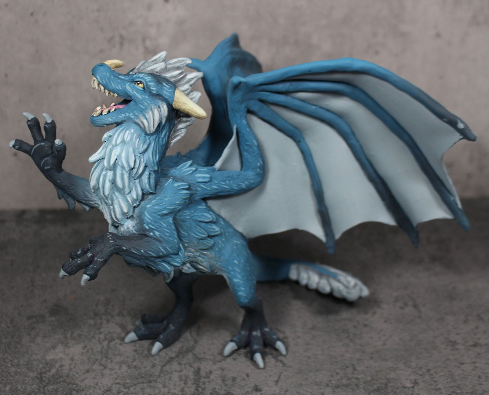 A sculpture of a furry dragon rearing on his hind legs and pawing at the air.  He is blue with a white underside and dark tipped feet.  His mane and wings are silver.