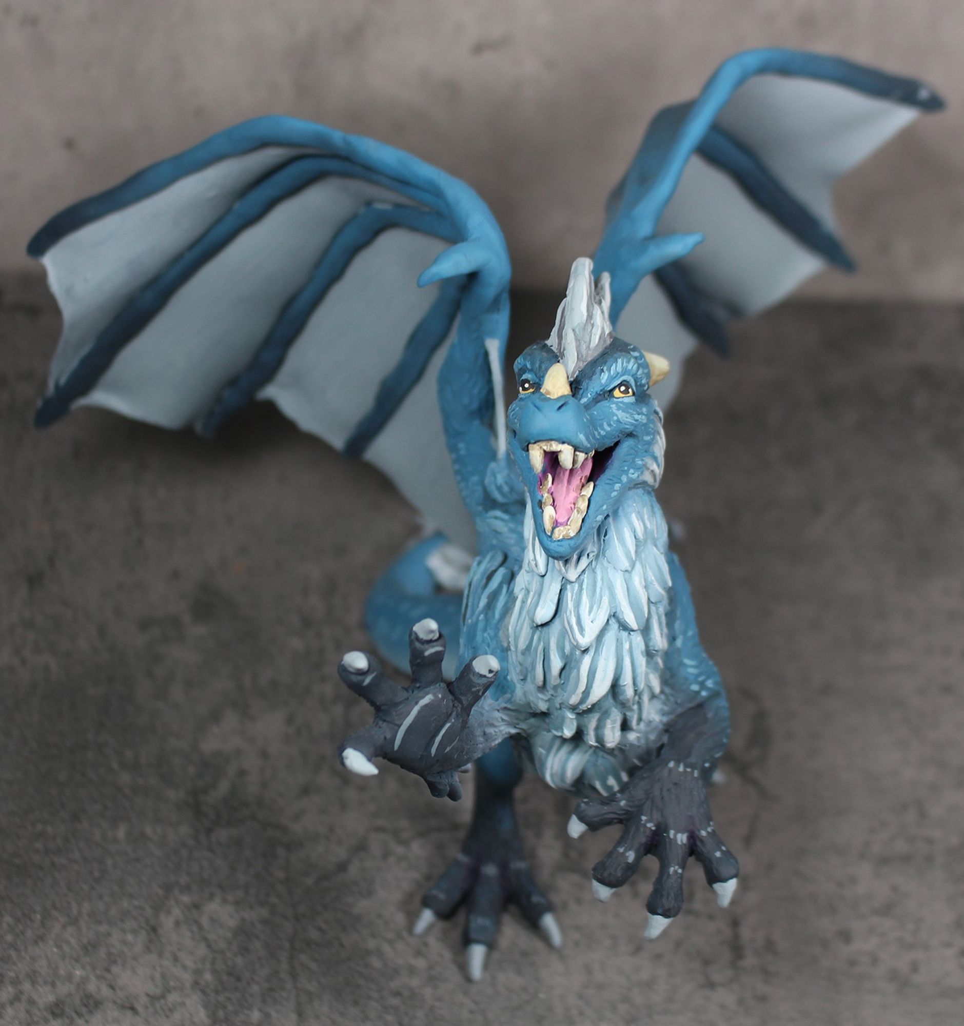 Top view - A sculpture of a furry dragon rearing on his hind legs and pawing at the air.  He is blue with a white underside and dark tipped feet.  His mane and wings are silver.