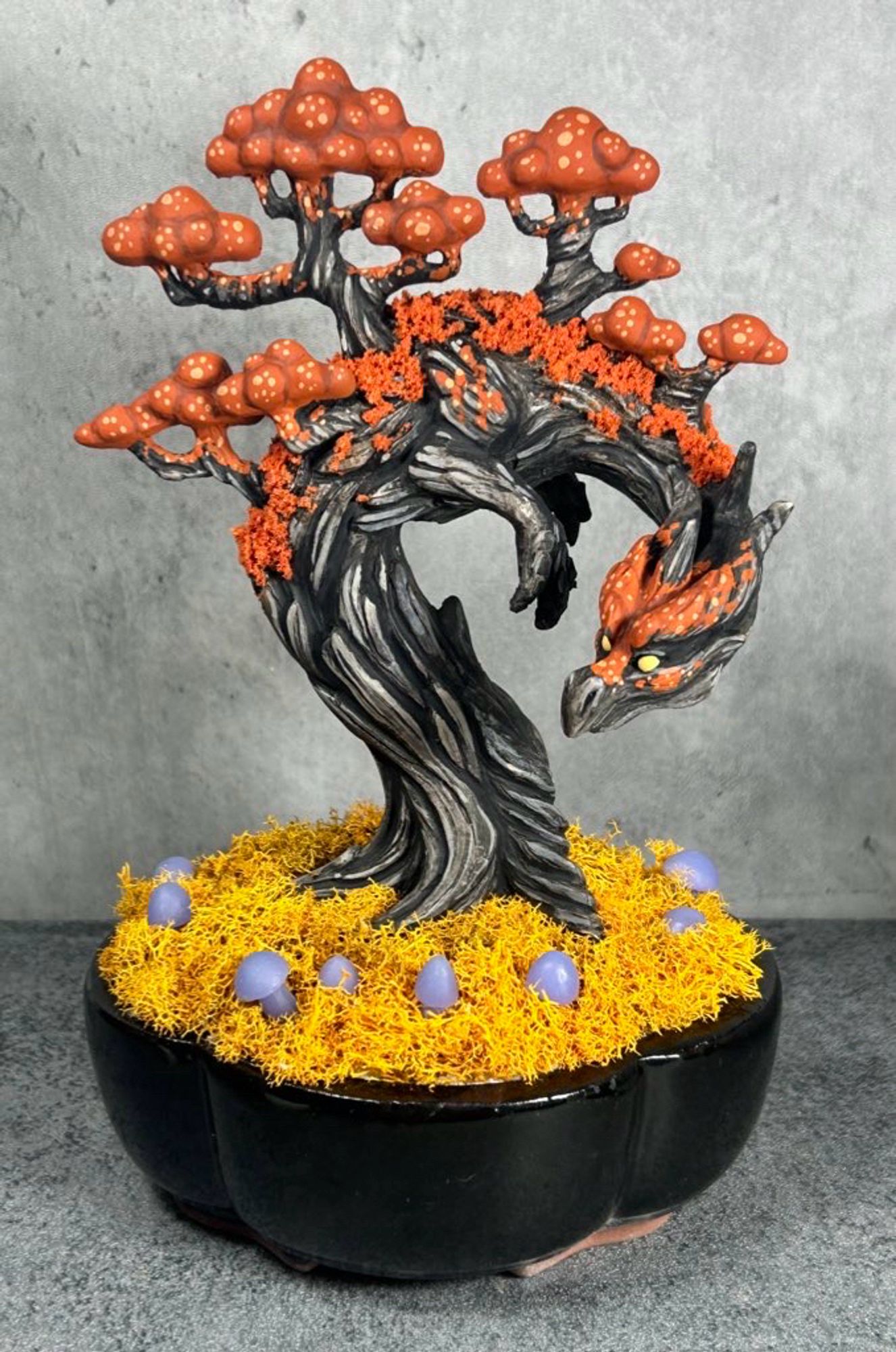 A black and orange Halloween themed tree dragon planted in a black pot surrounded by golden moss and purple mushrooms.