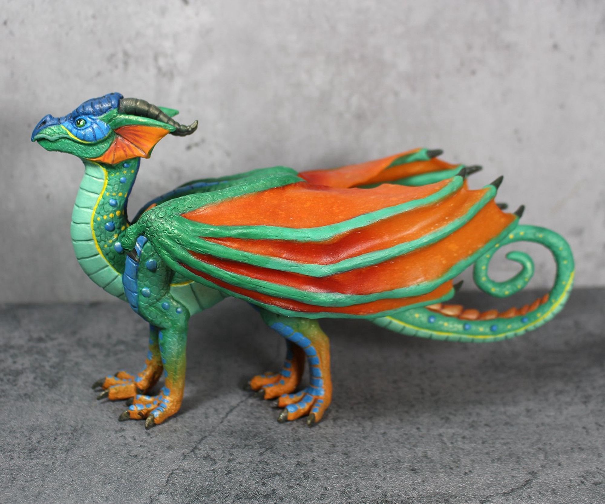 A sculpture of the dragon Glory from Wings of Fire. She is brightly colored with green scales and orange wings.