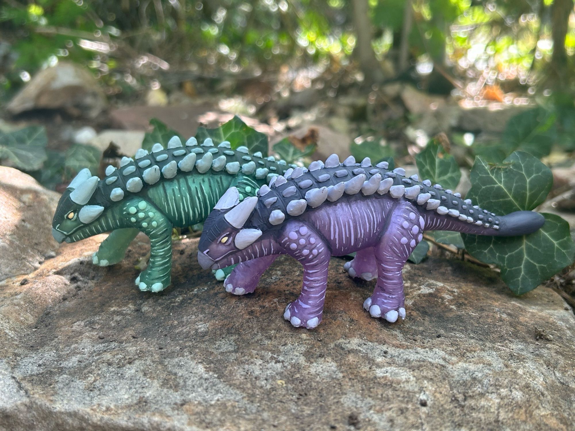 Two ankylosaurus sculptures, one green and one purple, standing on rock.