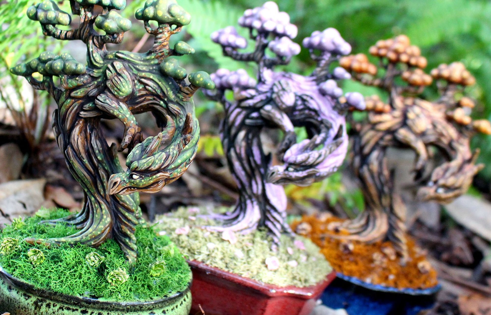 Three tree dragon sculptures planted in pots.  From front to back they are colored like the seasons summer (green), spring (pink), and autumn (orange).