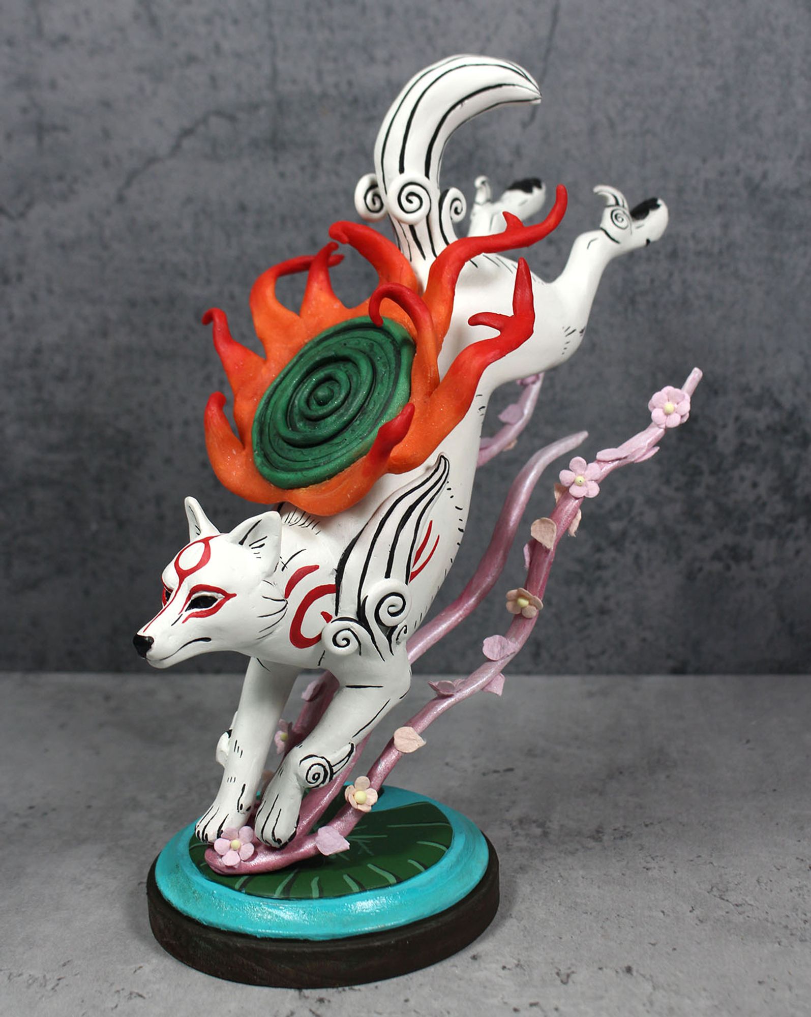 A sculpture of the white wolf Amaterasu from the game Okami.  She is leaping down onto a lily pad, kicking up swirls of cherry blossoms behind her.