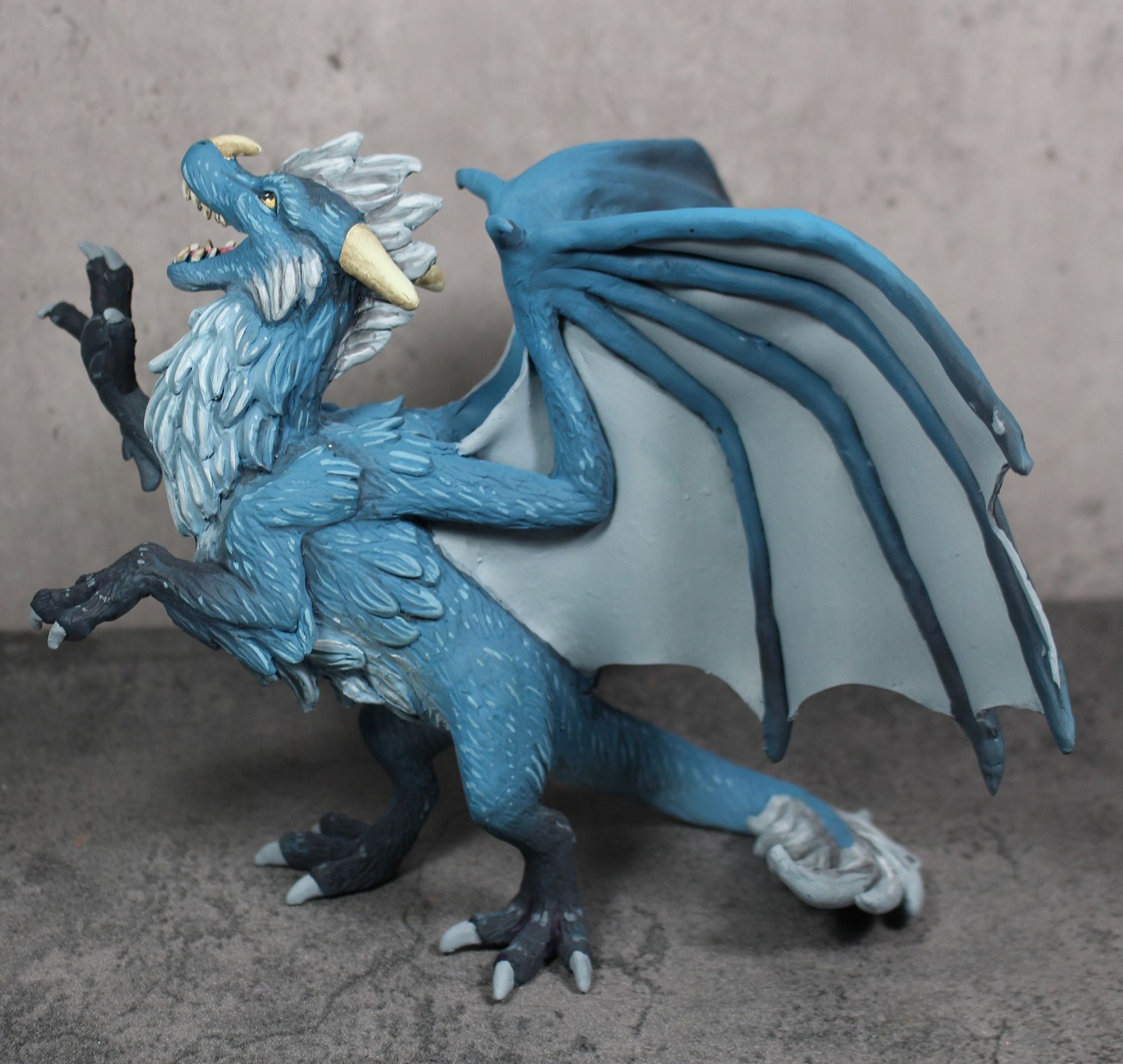 Side view - A sculpture of a furry dragon rearing on his hind legs and pawing at the air.  He is blue with a white underside and dark tipped feet.  His mane and wings are silver.