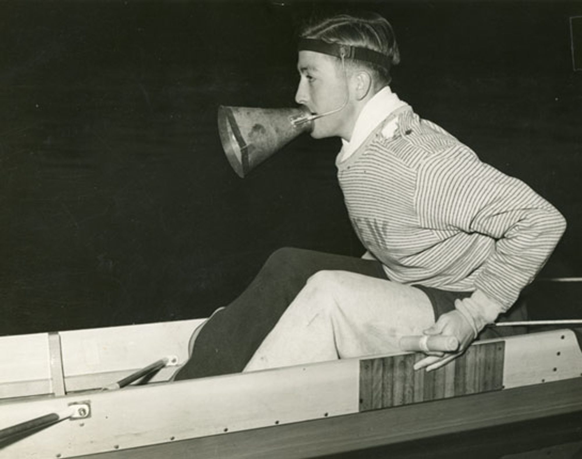 Coxswain in a crew boat wearing a cool megaphone thing on his head.