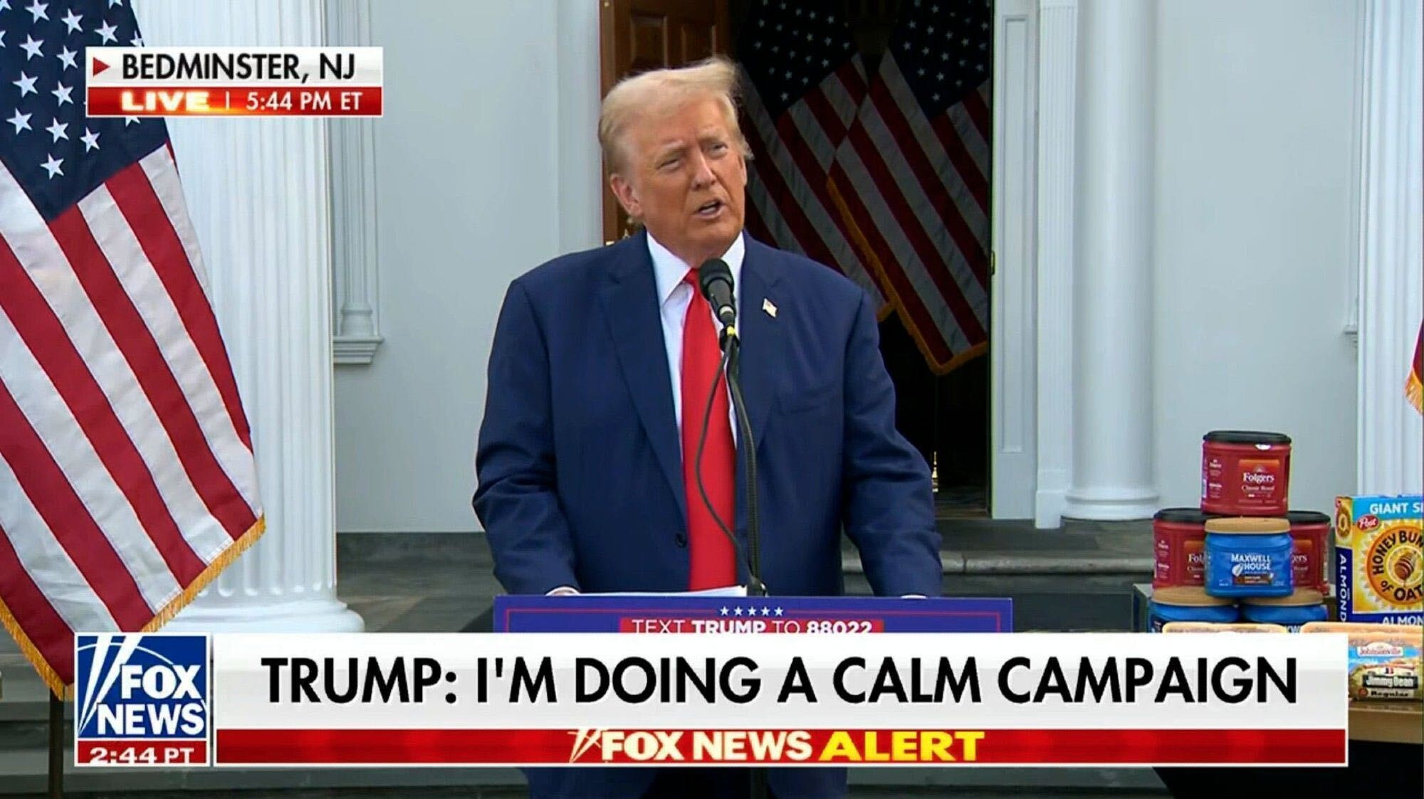 A screenshot of Fox News depicting Donald Trump looking kind of honeybaked and vague in front of a pile of groceries outside his golf course in Western NJ. The chyron reads "Trump: I'm Doing A Calm Campaign."