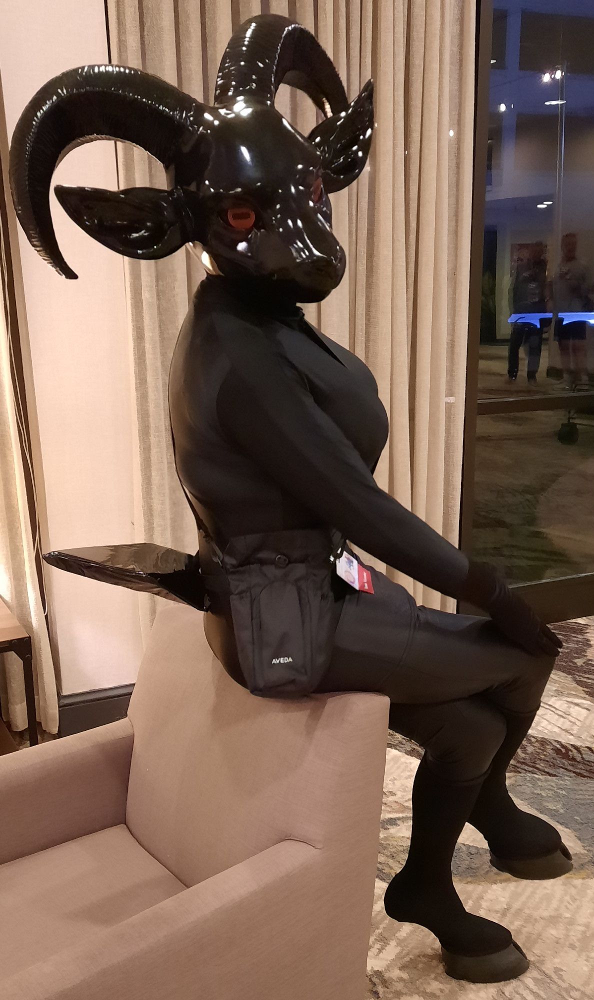 Onyx appearing as an all black and shiny anthro goat with red eyes and realistic goat hooves.  Perched on a seatback, you can see her flippy tail.