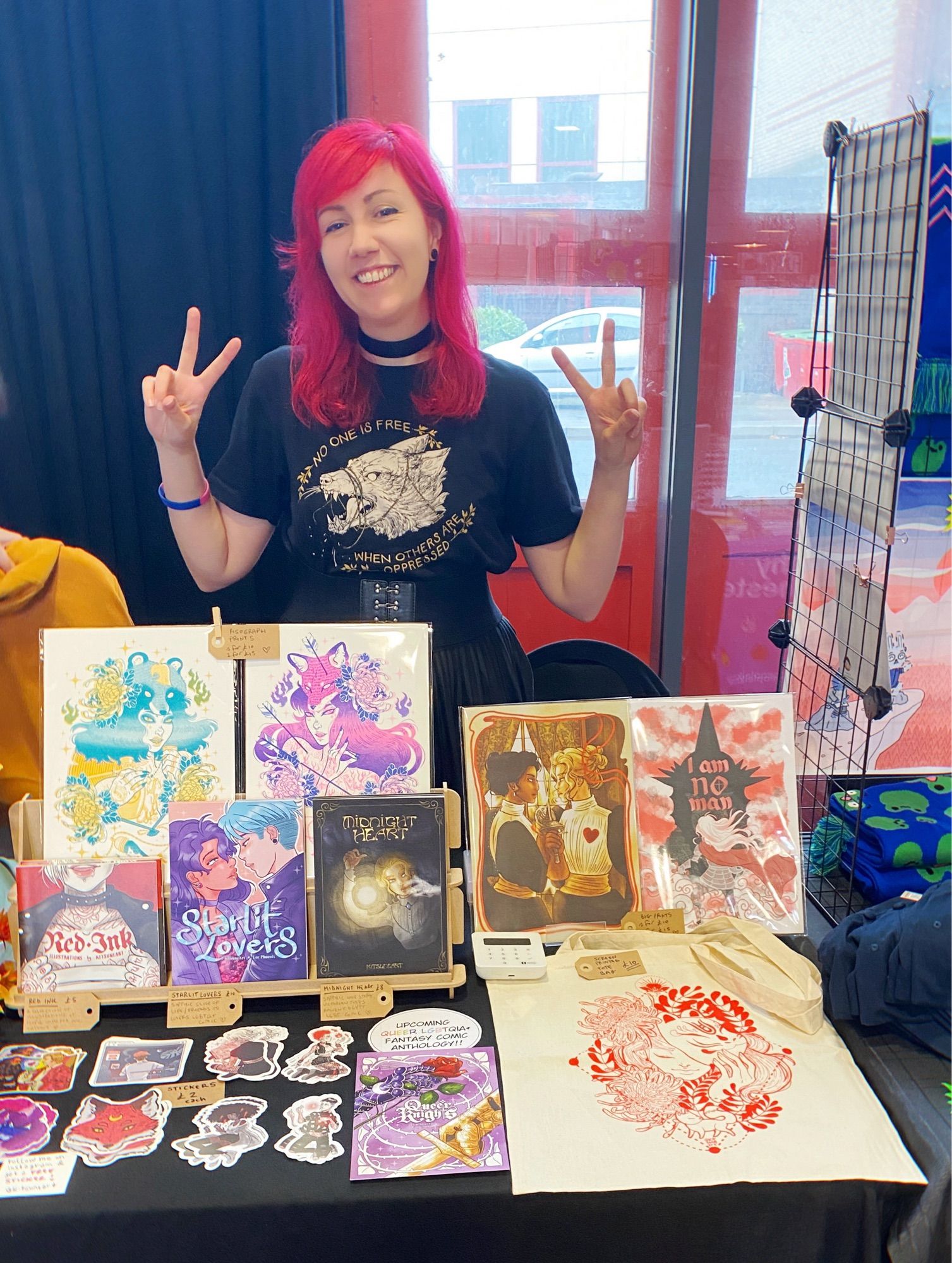 Kitsuneart in front of her table at Pride Comic Art Festival. On display her comics, her latest risograph prints, stickers and tote bag