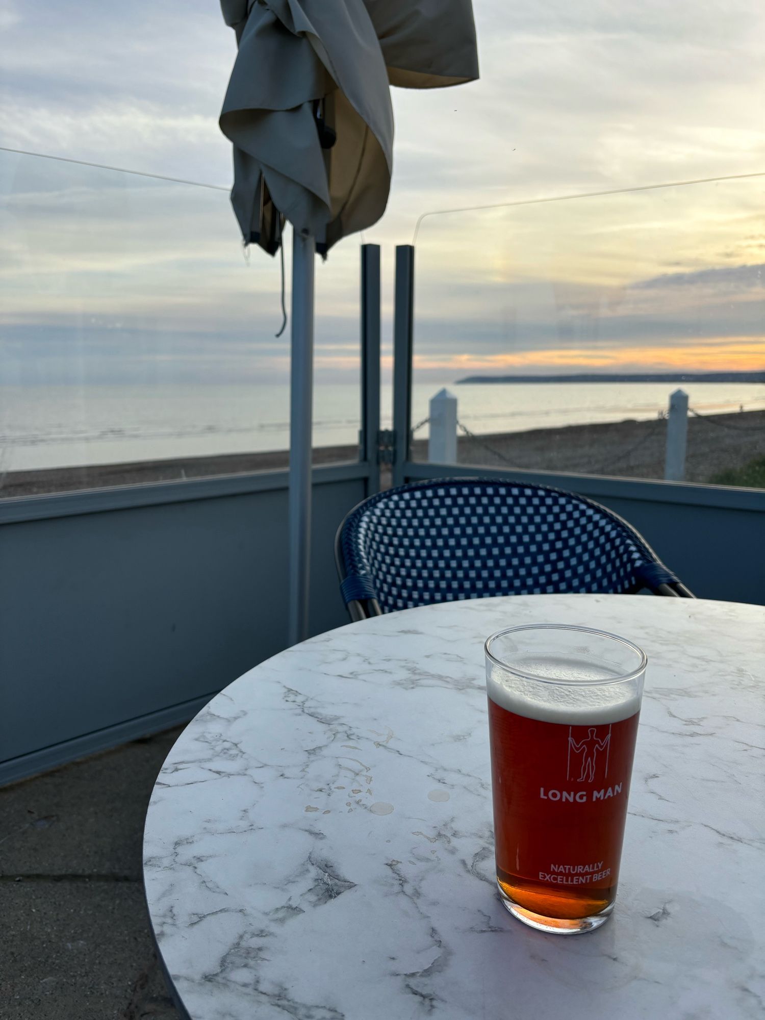 A pint of Long man best bitter on a table with the sea and coast in the background as the sun is getting lower in the sky. Derp deserves at least another couple of pints.