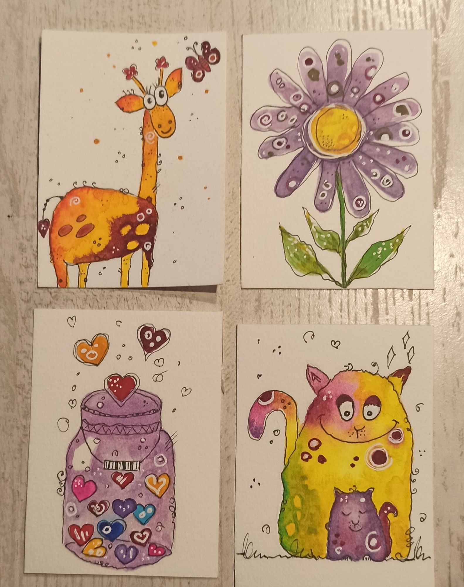 Vier ATC mit Happypainting-Motiven:
Oben: eine Giraffe und eine lila Blume. 
Unten: ein Glas mit vielen bunten Herzen, eine Katzenmutter mit ihrem Kind.