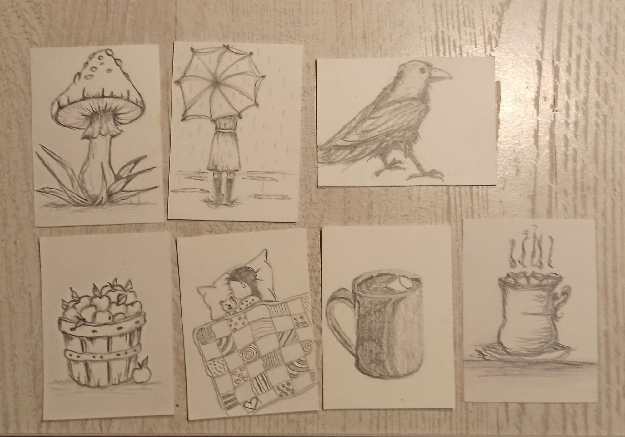 7 ATC mit Bleistift gezeichnet. 
Obere Reihe: Fliegenpilz, Mädchen im Regen mit Regenschirm, Krähe. 
Untere Reihe: ein Korb mit Äpfeln, ein kleines Mädchen mit Teddy unter einer Patchworkdecke, Tasse Kakao mit einem Marshmallow, Tasse Kakao mit Marshmallows.