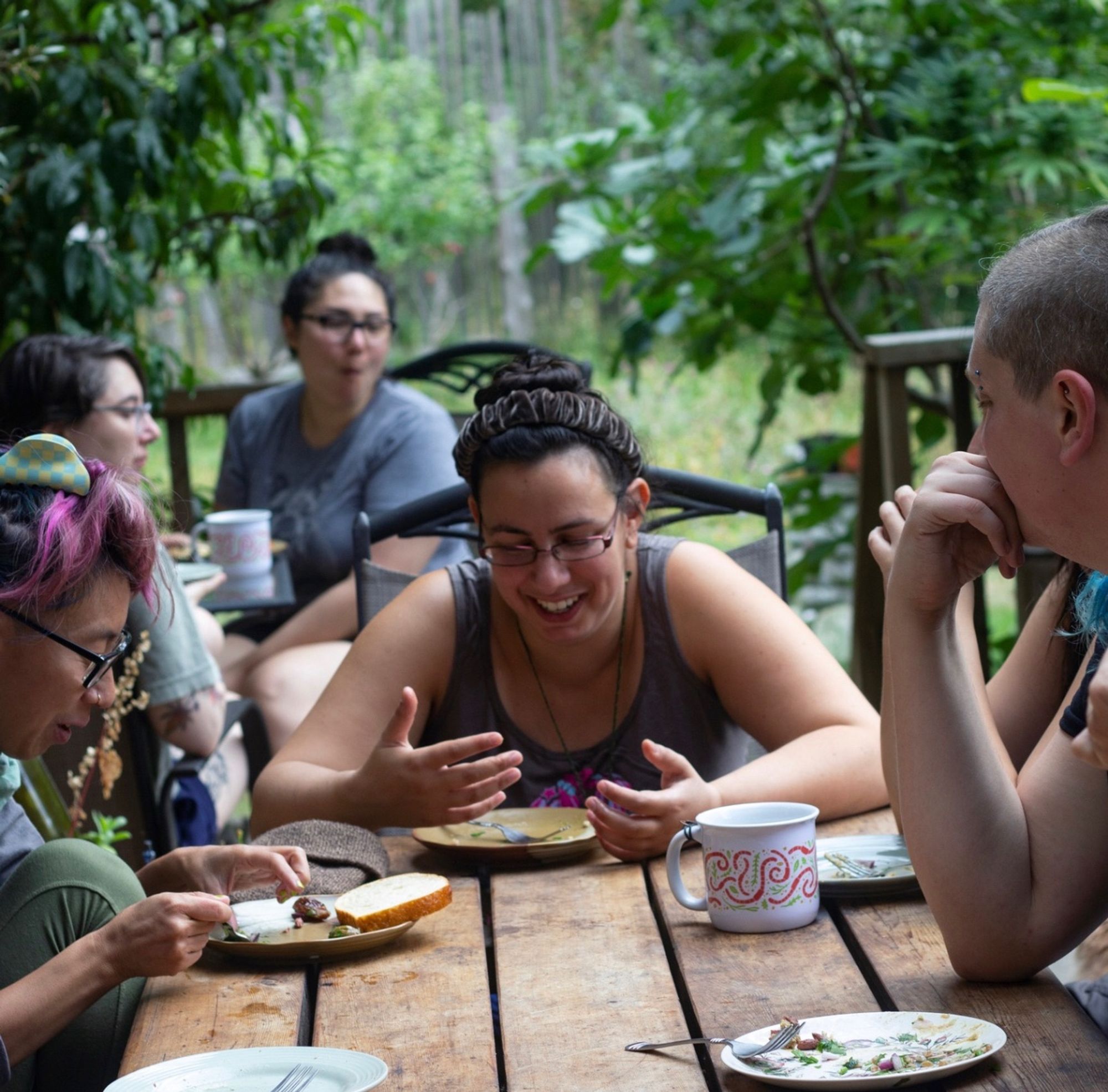 Retreats laugh and talk around lunch on a wooden outdoor table.