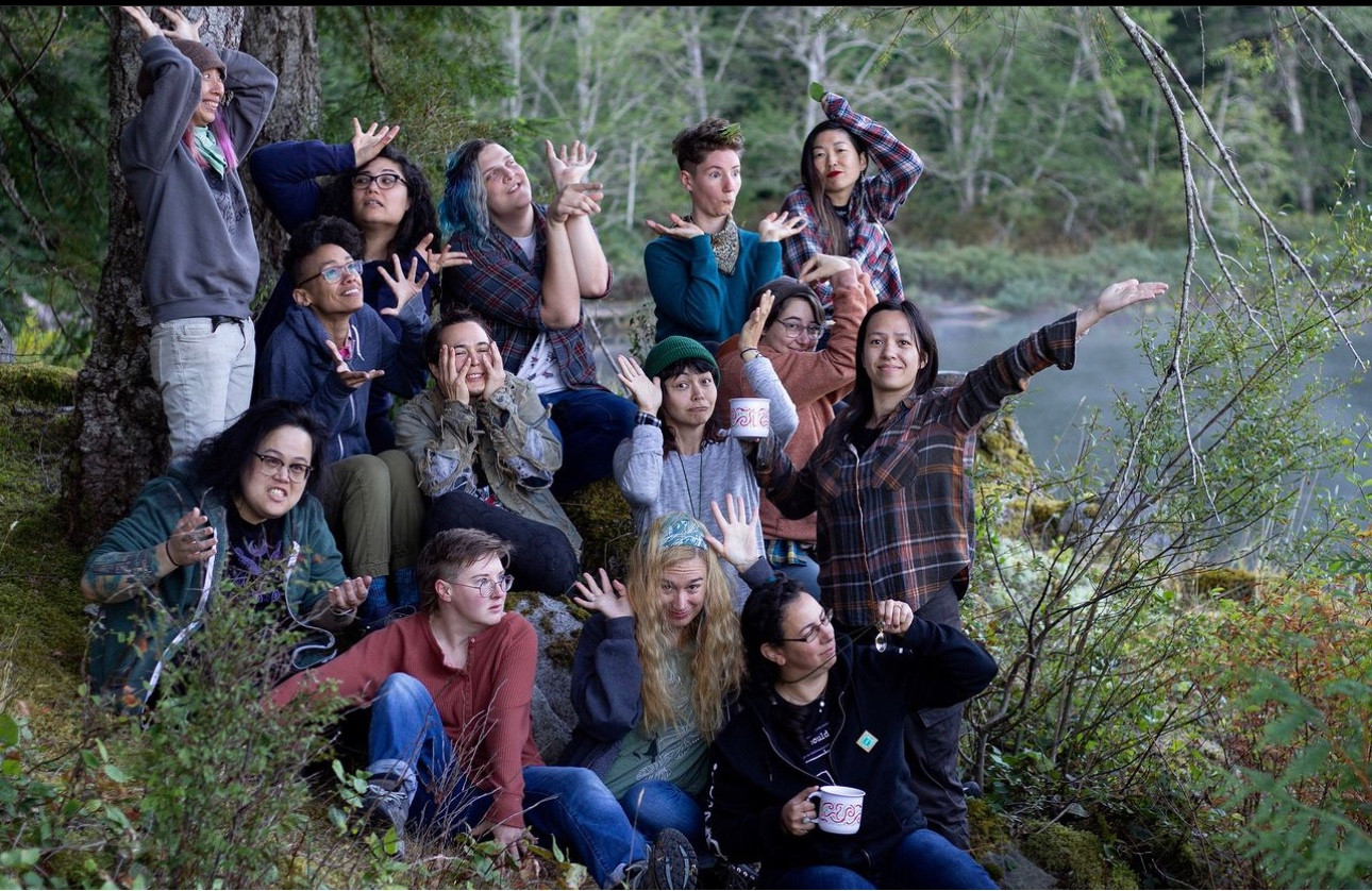 A group photo of retreaters by a lake, posing to a prompt along the lines of “be a sprouting plant”