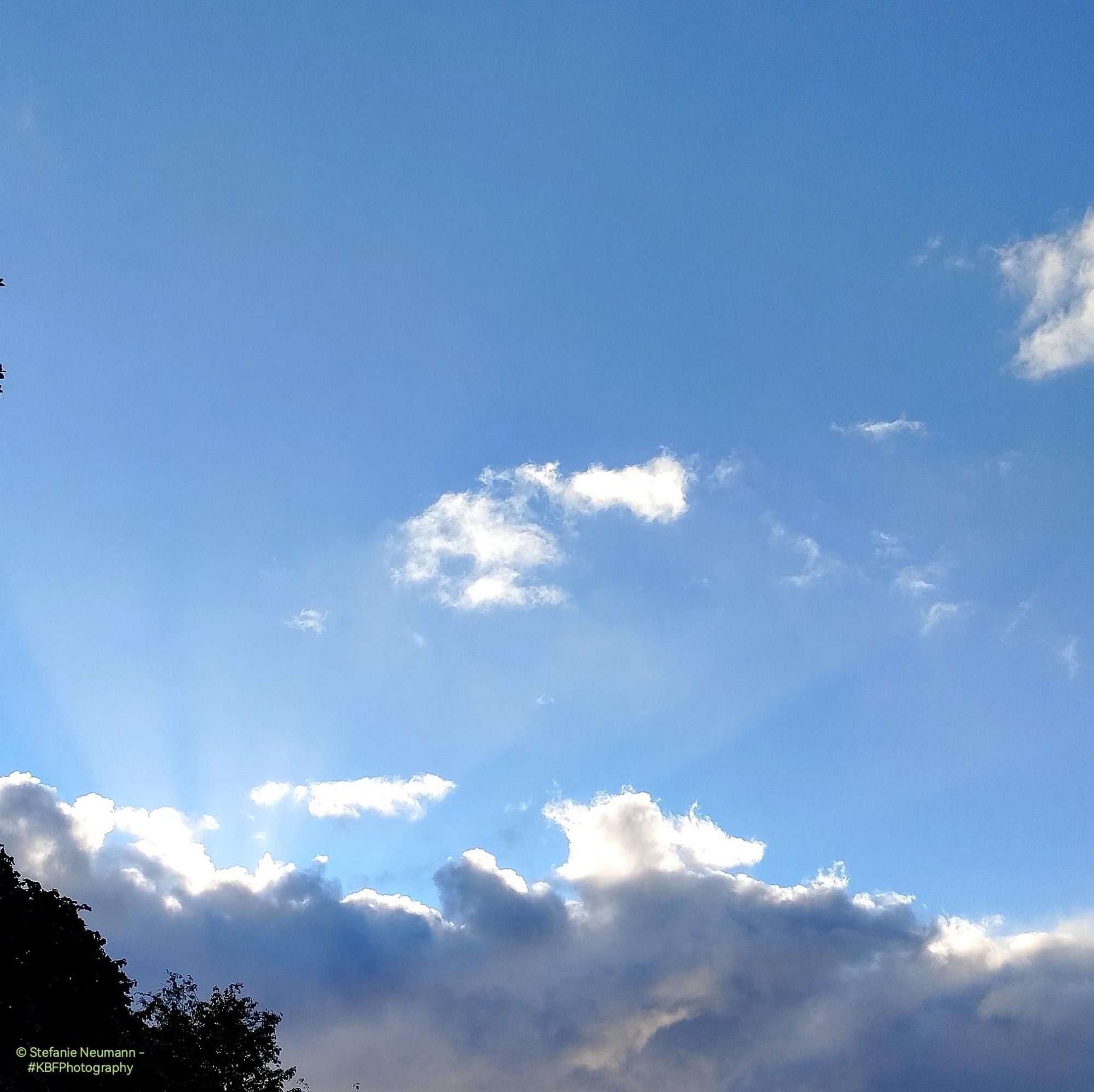 Sun rays blasting into the blue sky from behind dark rain-clouds.