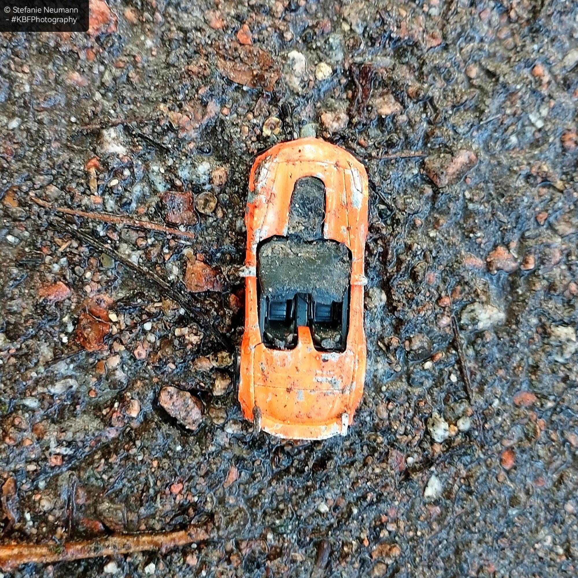 A little, dirty, orange toy car on wet, sandy ground.