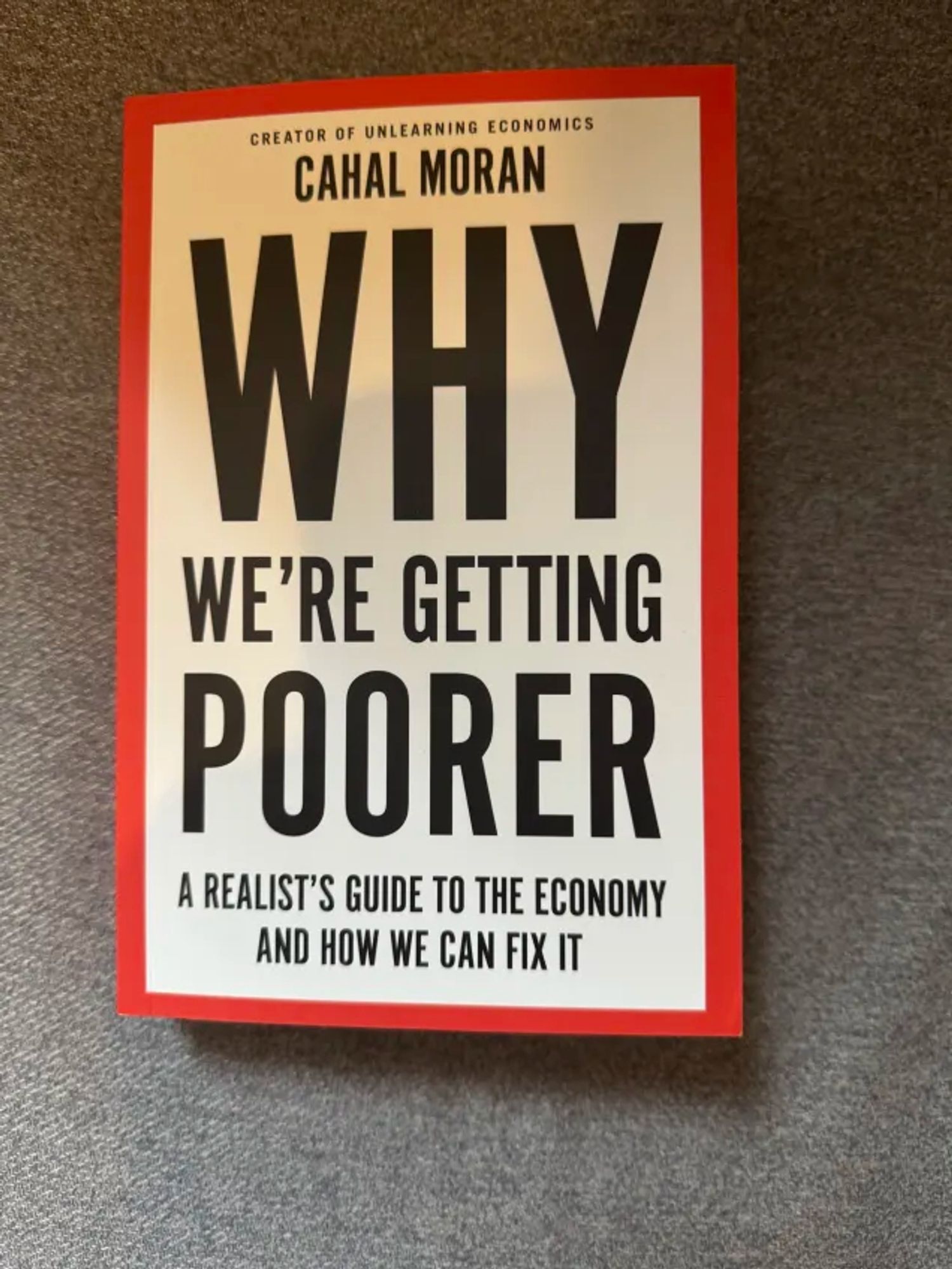 My book Why We're Getting Poorer: A Realist's Guide to the Economy and How We Can Fix It. Written by Cahal Moran/Unlearning Economics. The book cover is white with a red border and bold black font for the title/author/subtitle.