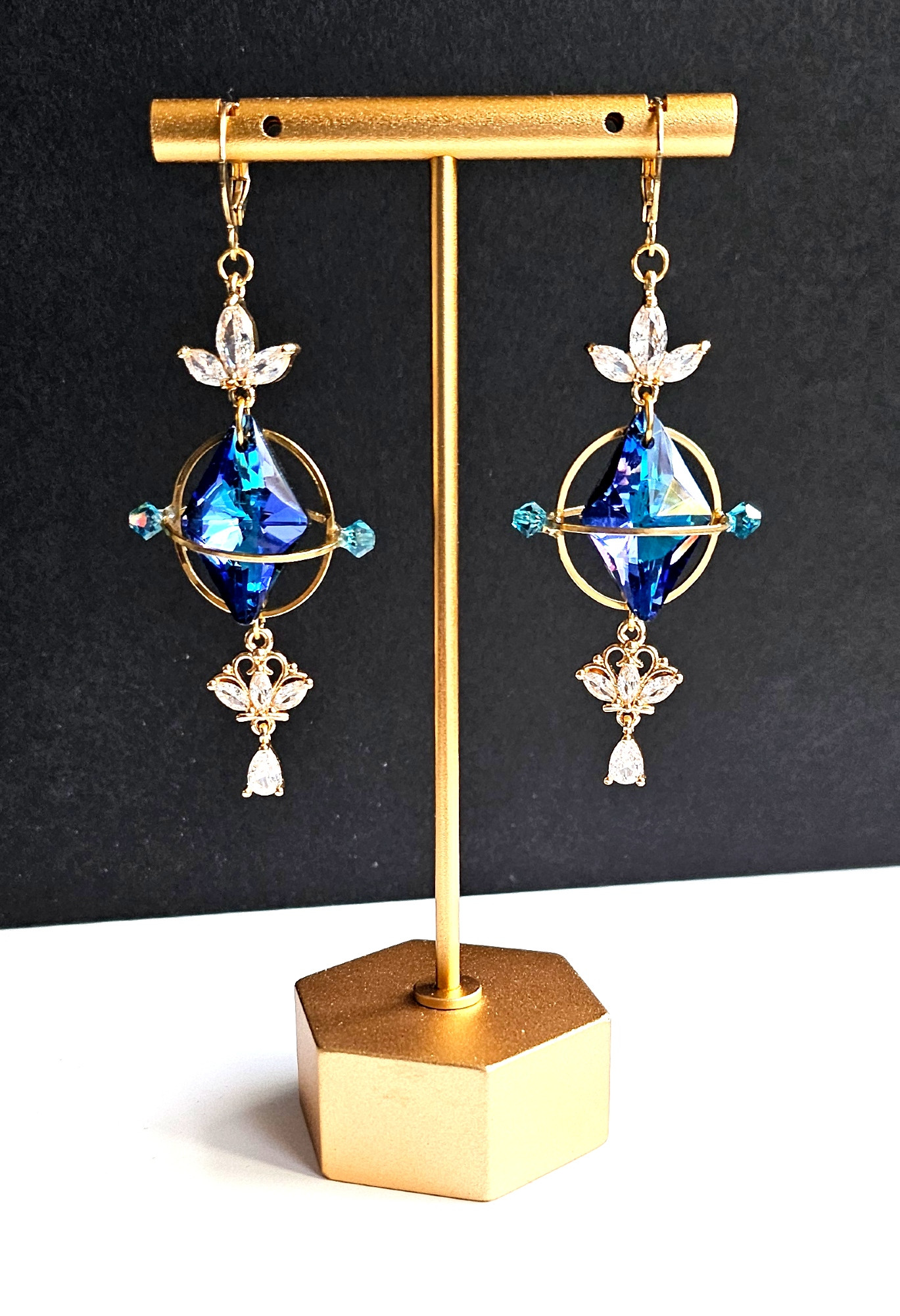 a pair of golden earrings looking like aetherytes with blue crystals and little white crystals inspired from the game final fantasy 14
