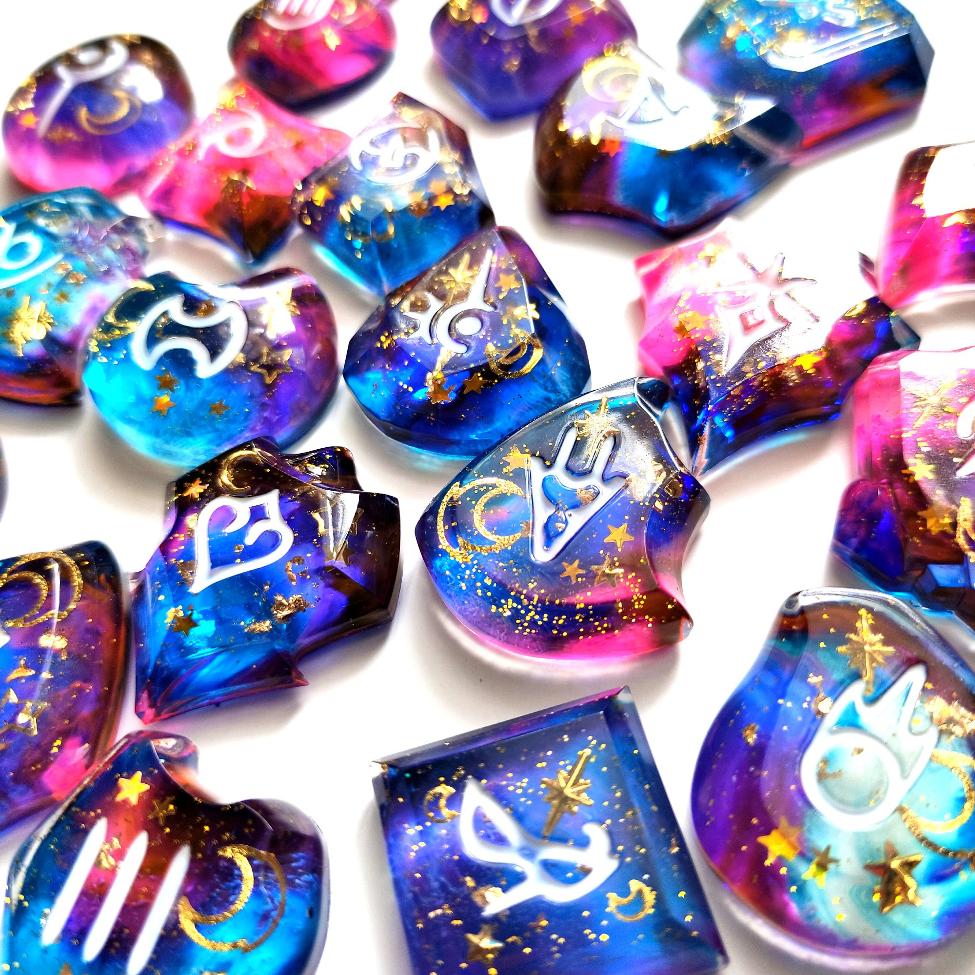 Zoom photo of resin job stones from the game final fantasy 14. They are blue, pink and purple with gold stars, moons and glitter.